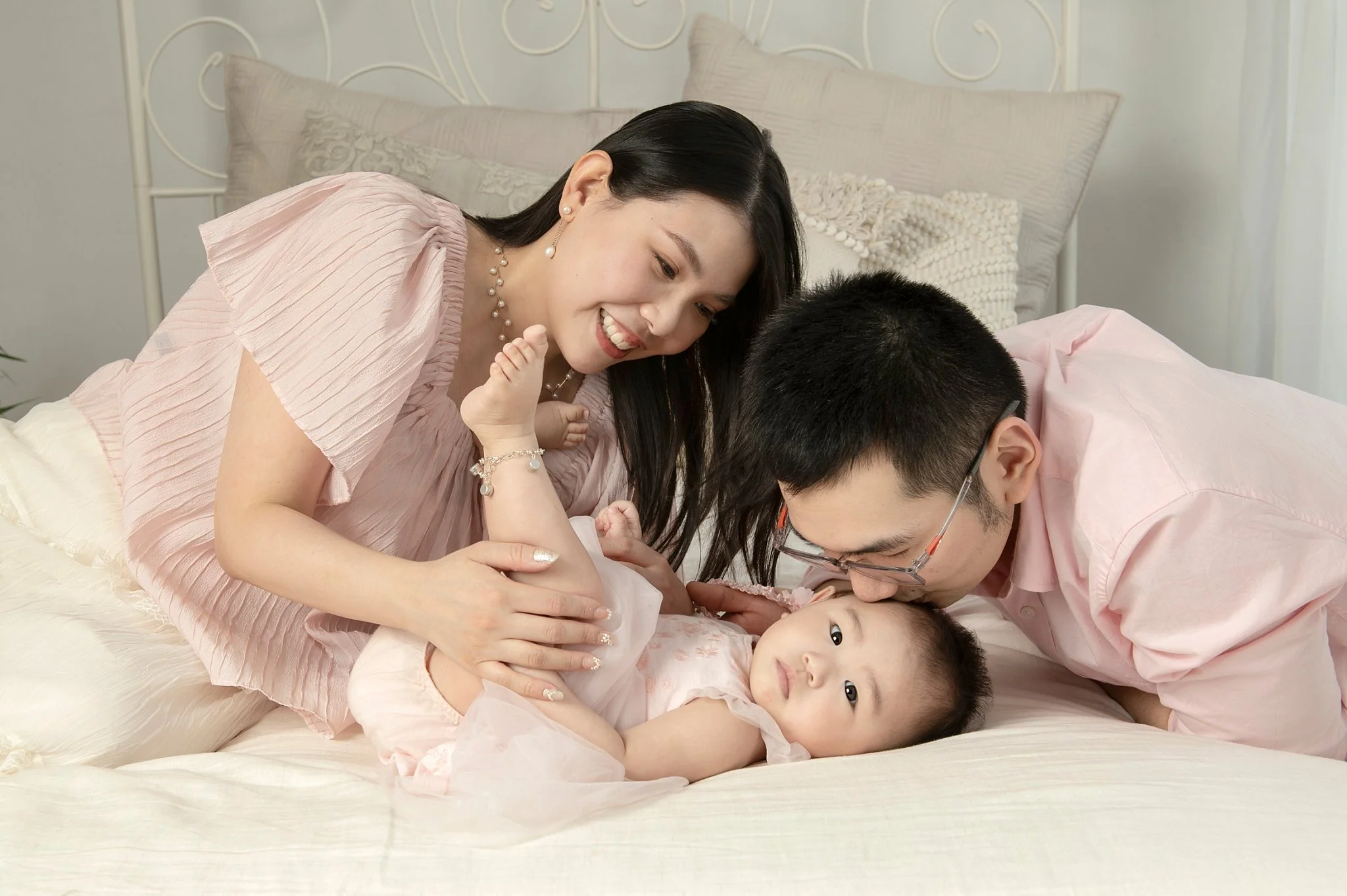 Mum and dad leaning over their baby on a white bed during a baby studio session on Sydney's North Shore