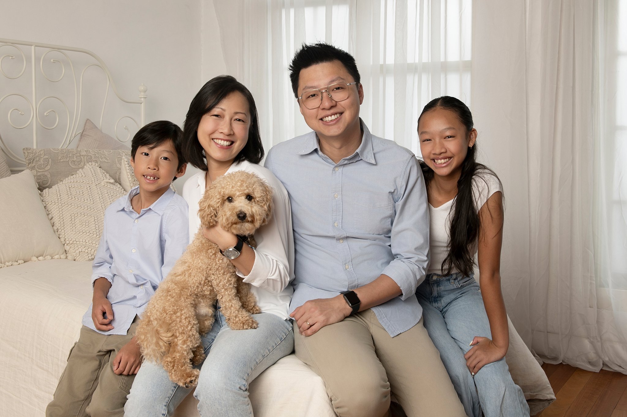 Family of four sitting together in a studio with a small cavoodle on mum's lap, all in soft blue tones