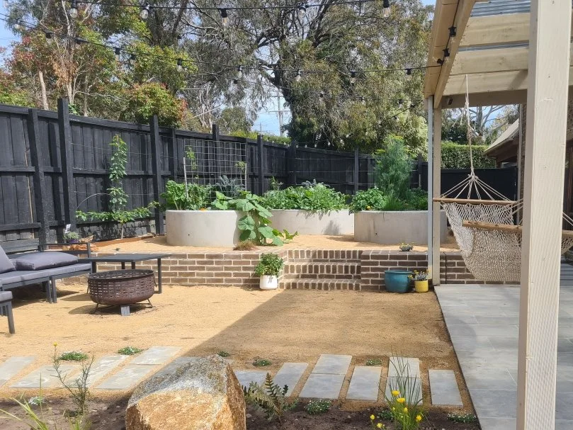 Mornington Peninsula, Mount Martha backyard garden with raised round concrete beds, crushed rock paths, a black fence and a hammock on the porch. Designed by Sheoak Design.