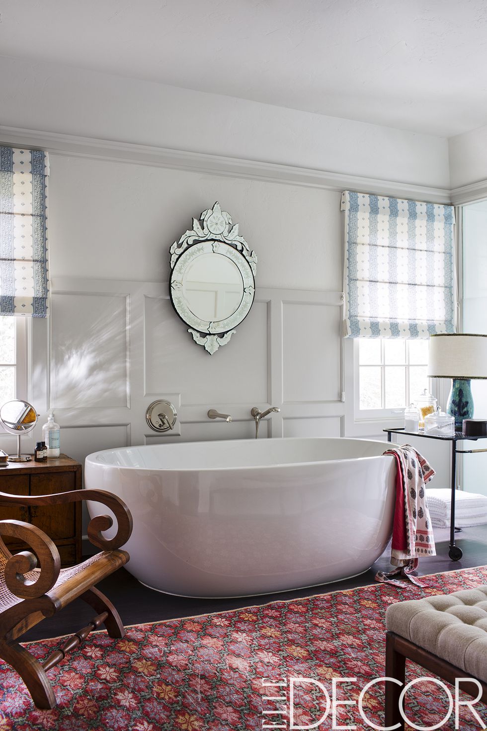 The master bath features a Venetian mirror, a 1950s bar cart by Mathieu Matégot , and a vintage rug, the flooring is oak and the walls are painted in Benjamin Moore’s Navajo White .