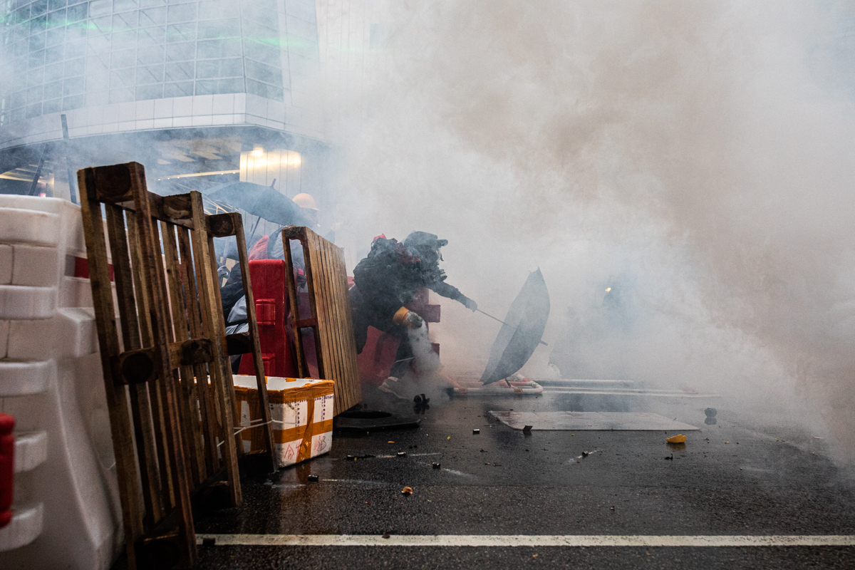 19.08.25 - Protestor emerges from the barricades to toss back a tear gas can.