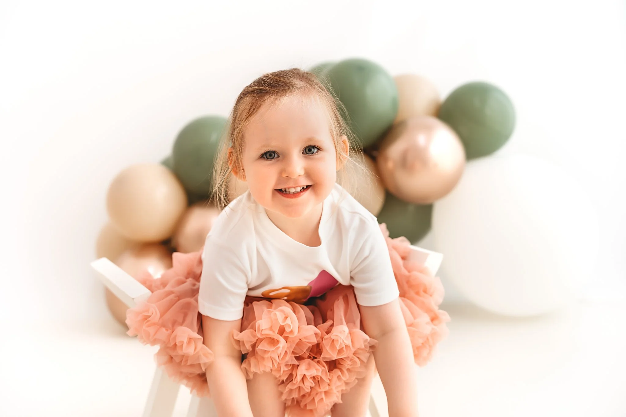 girl smiling in a pink tutu with sage green balloons in the background