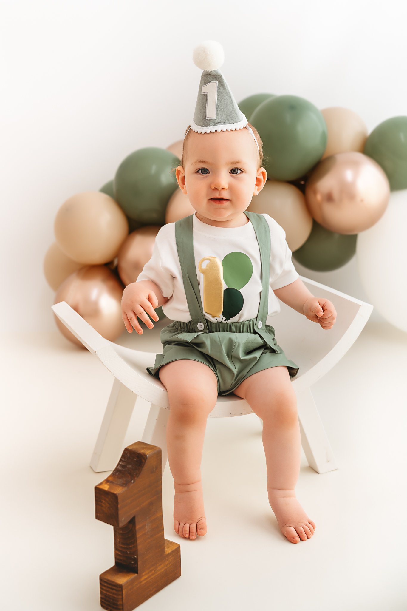 boy with birthday hat on set on a white bench with a number 1 block