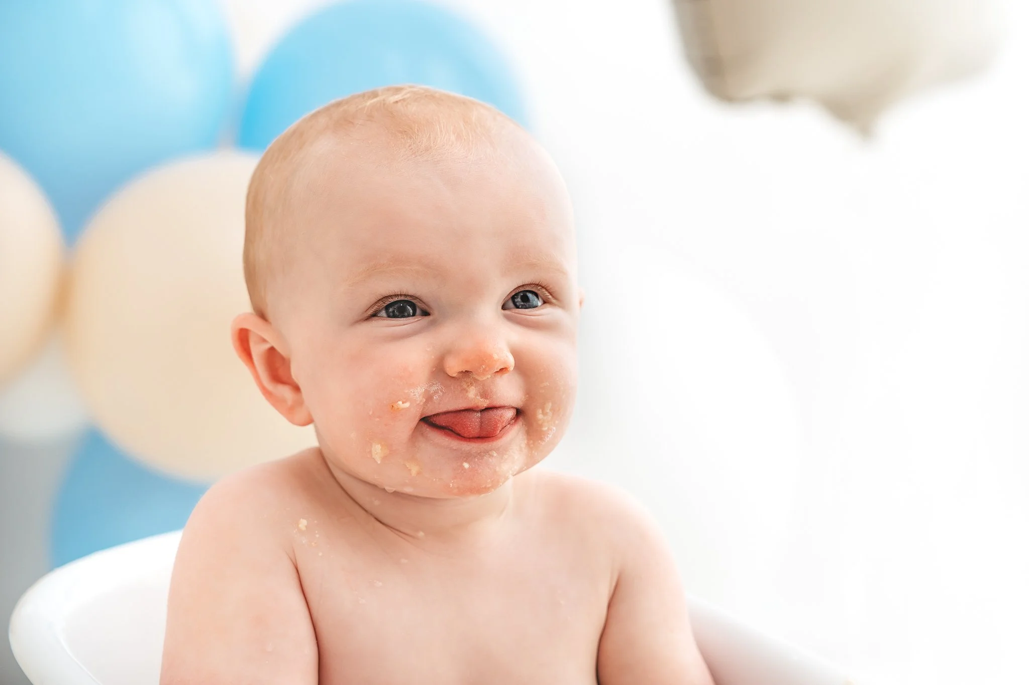 baby boy sticking tongue out with cake around his face