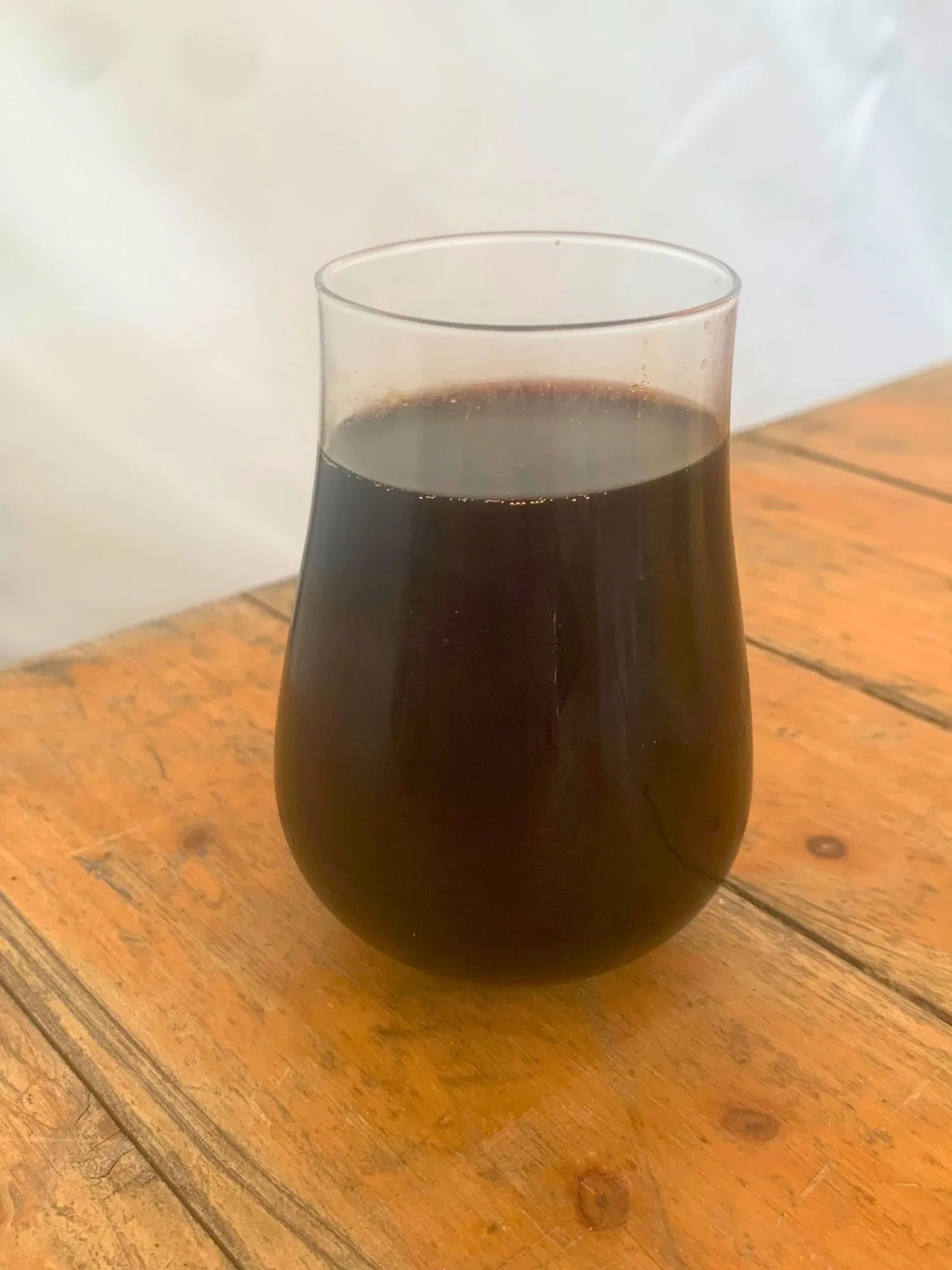 A dark, nearly black beer in a tulip-shaped glass on a rustic wooden table.