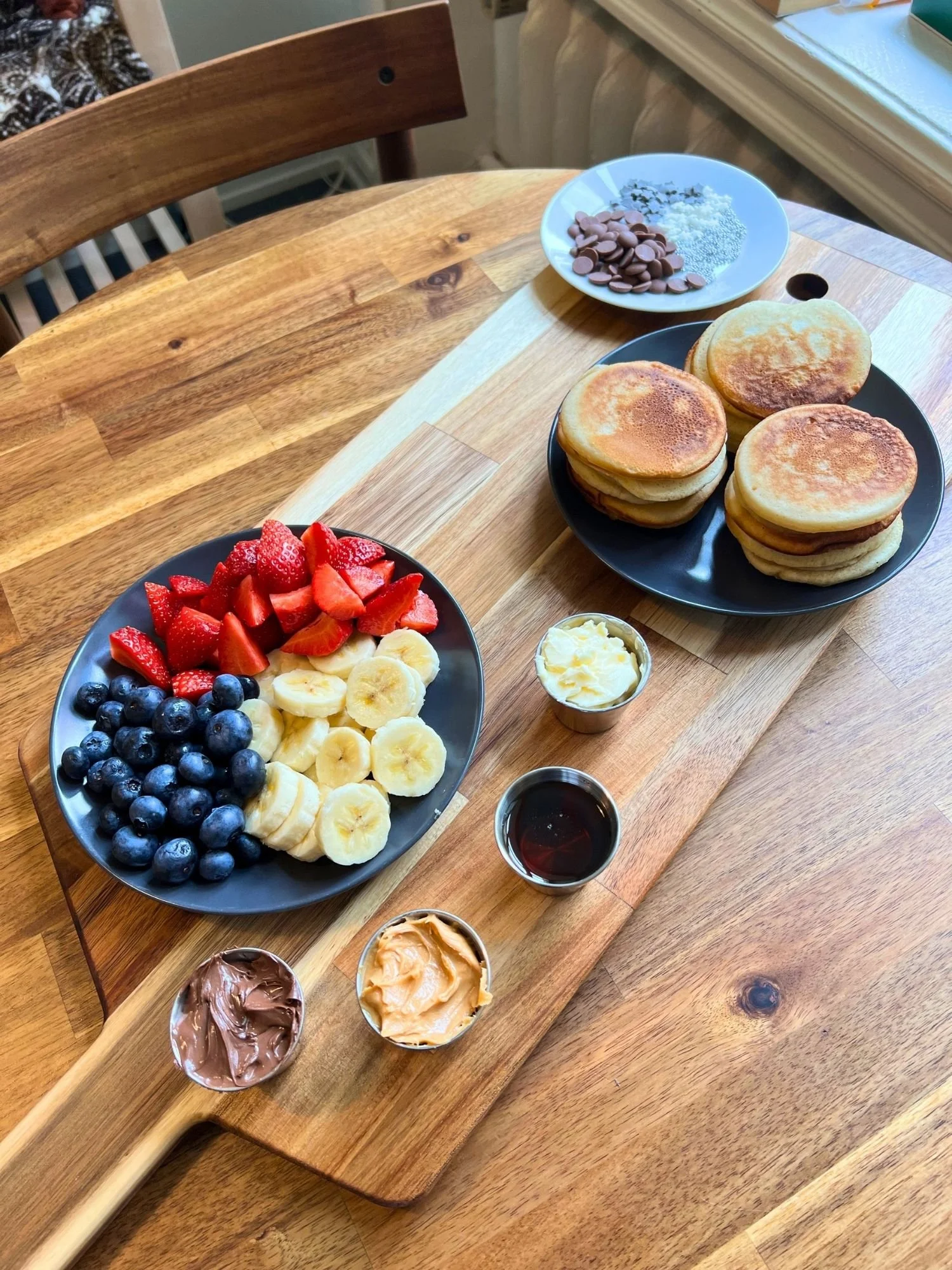 A wooden table setting featuring a breakfast board platter with stacks of golden mini pancakes.