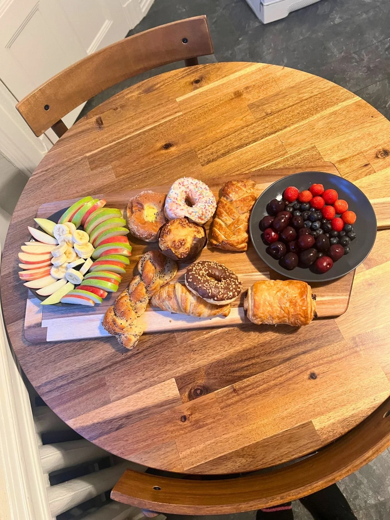 High-angle shot of a rectangular wooden serving board on a round wooden table, set with an assortment of sweet pastries.
