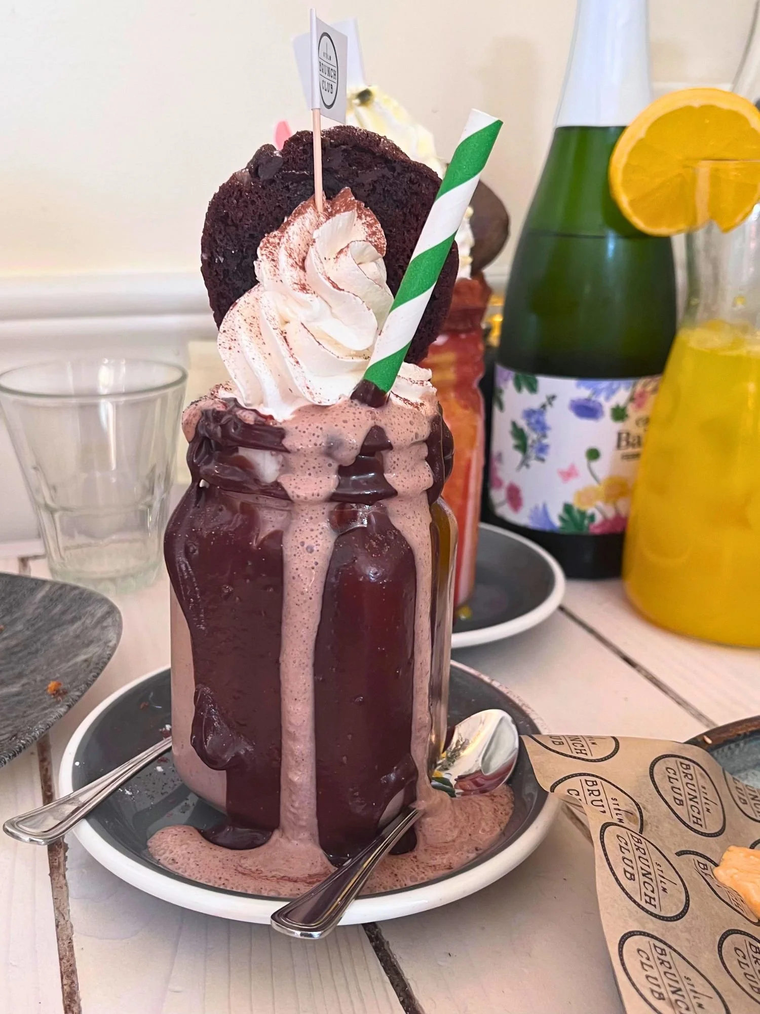 An overflowing chocolate freakshake in a mason jar with a striped straw topped with whipped cream and a large chocolate cookie.