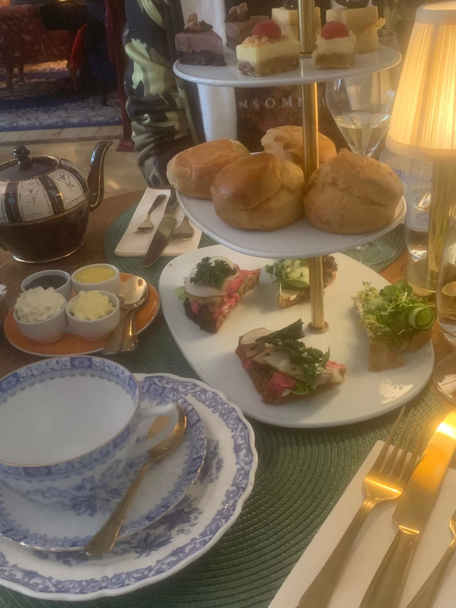 A three-tiered afternoon tea service on a table at Alice och Kattens Tesalong in Lund. The top tier has a variety of small cakes. This middle tier has four large, golden-brown scones.
