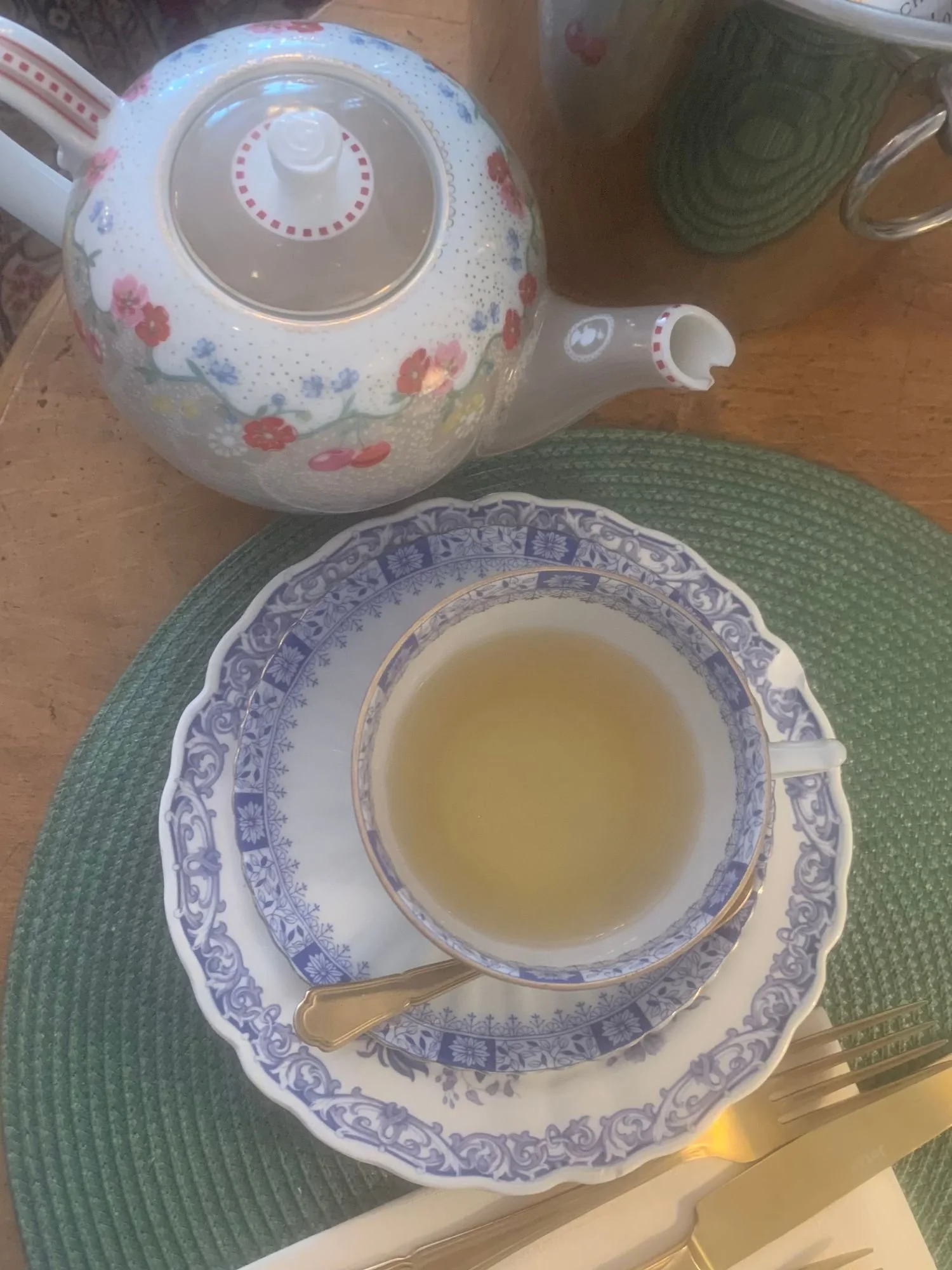 A tea setting on a wooden table at Alice och Kattens Tesalong in Lund. A delicate teacup filled with light-colored tea on a matching saucer and a larger plate, all featuring an intricate blue floral pattern.