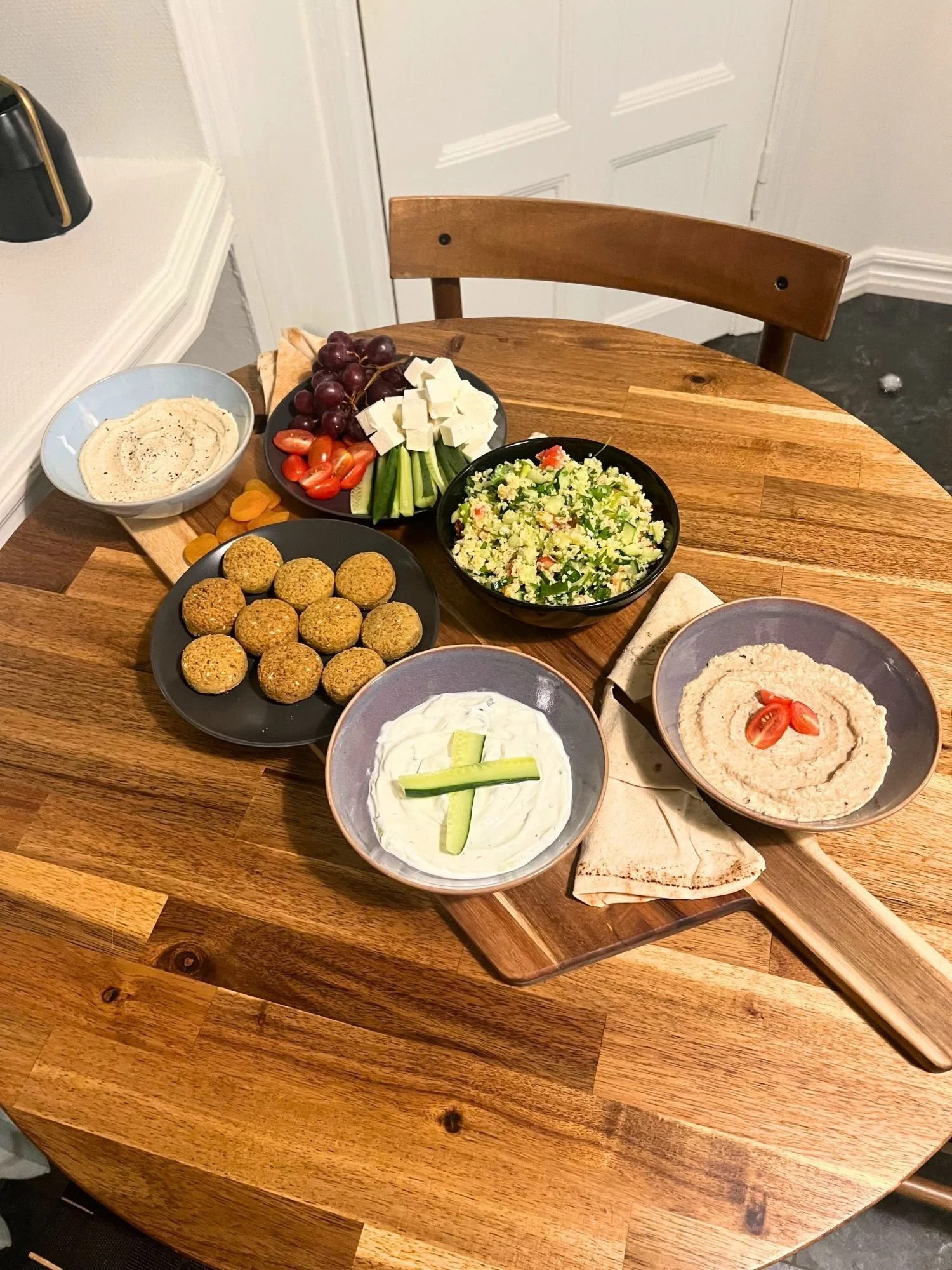 A round wooden table filled with a Mediterranean mezze spread arranged on a wooden cutting board.