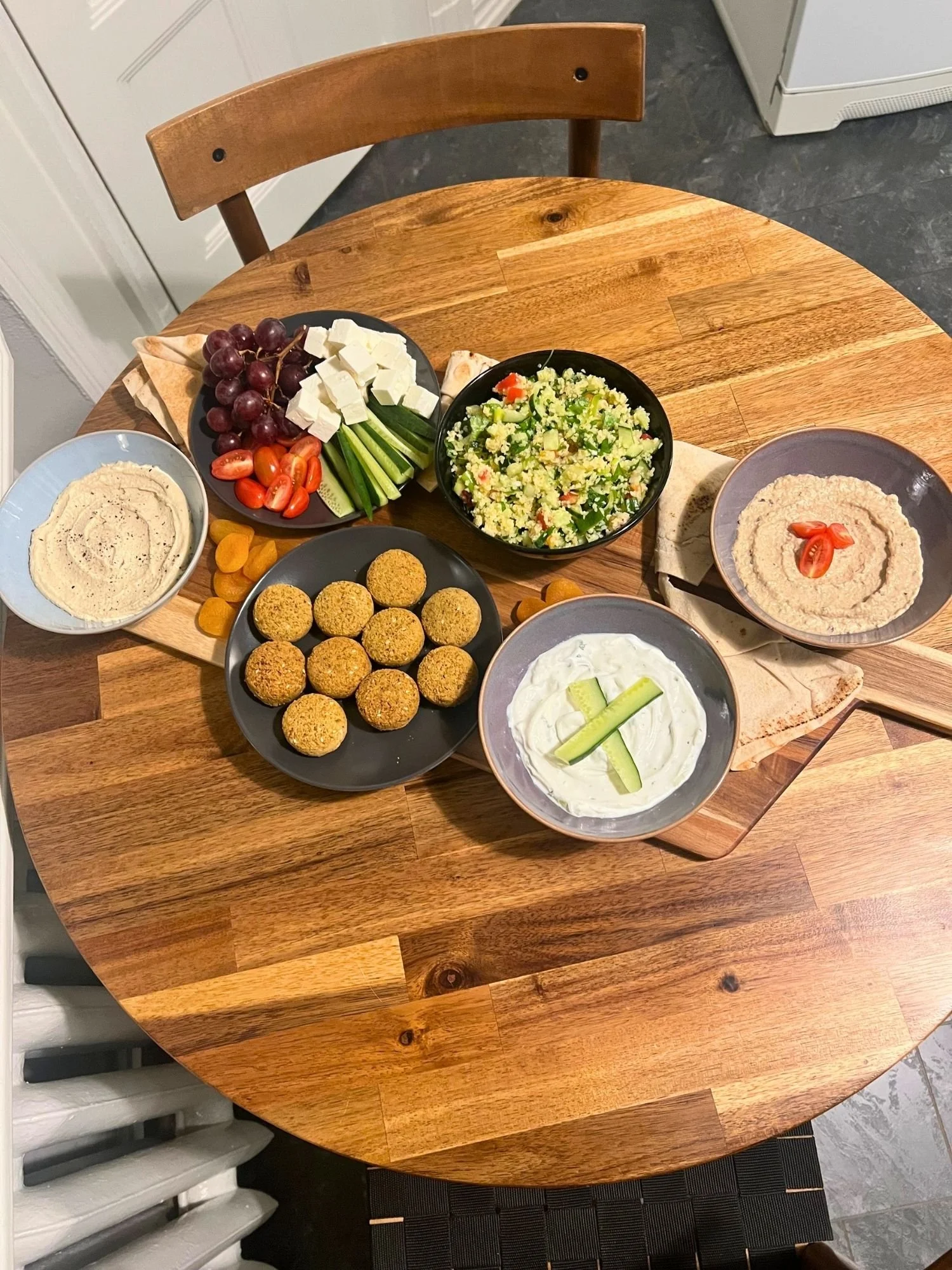 High-angle shot of a long wooden serving board on a round wooden table, set with a Mediterranean mezze spread.
