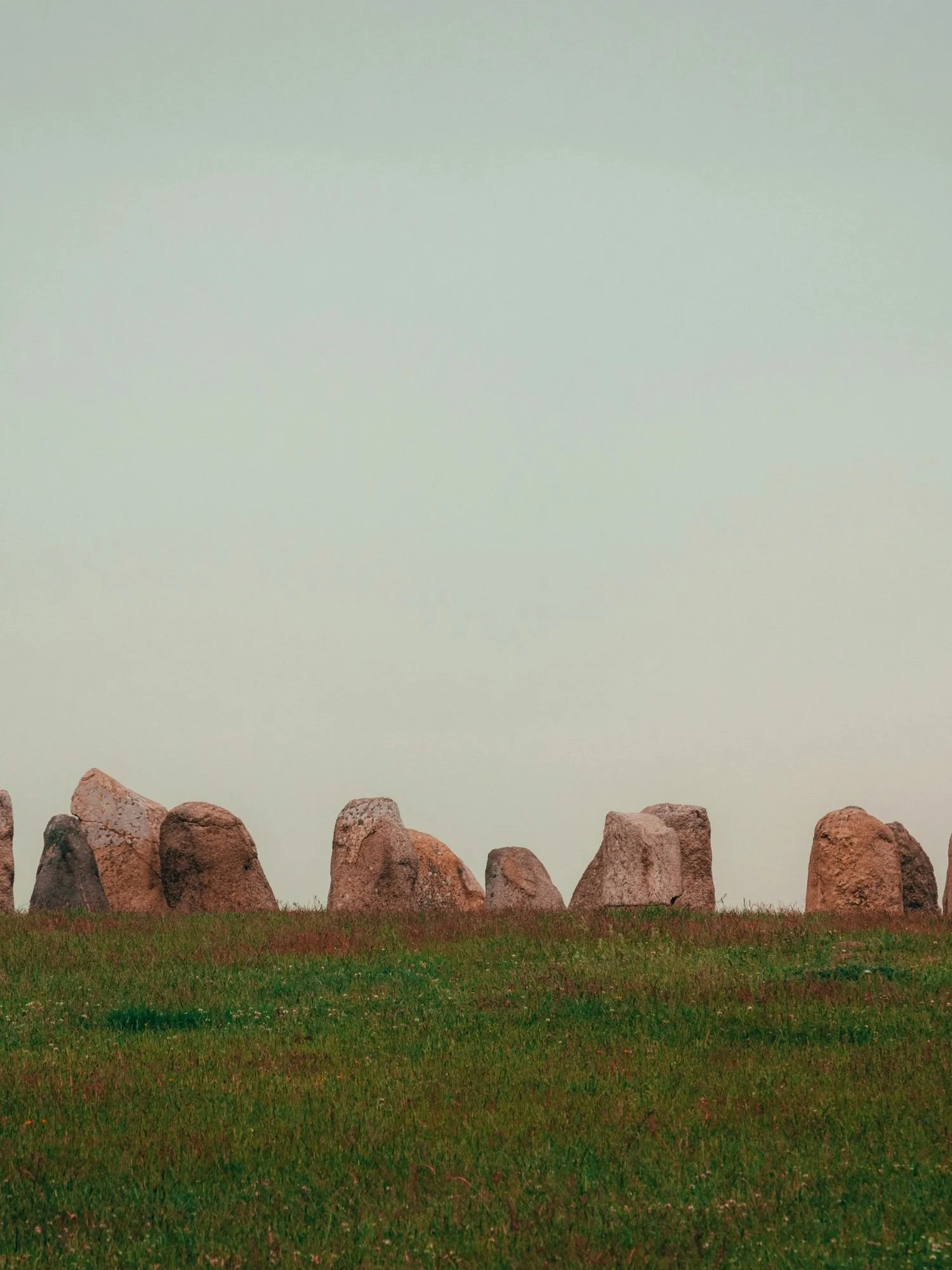 Ancient standing stones at Ales Stenar silhouetted on a grassy hill beneath a soft, misty sky.