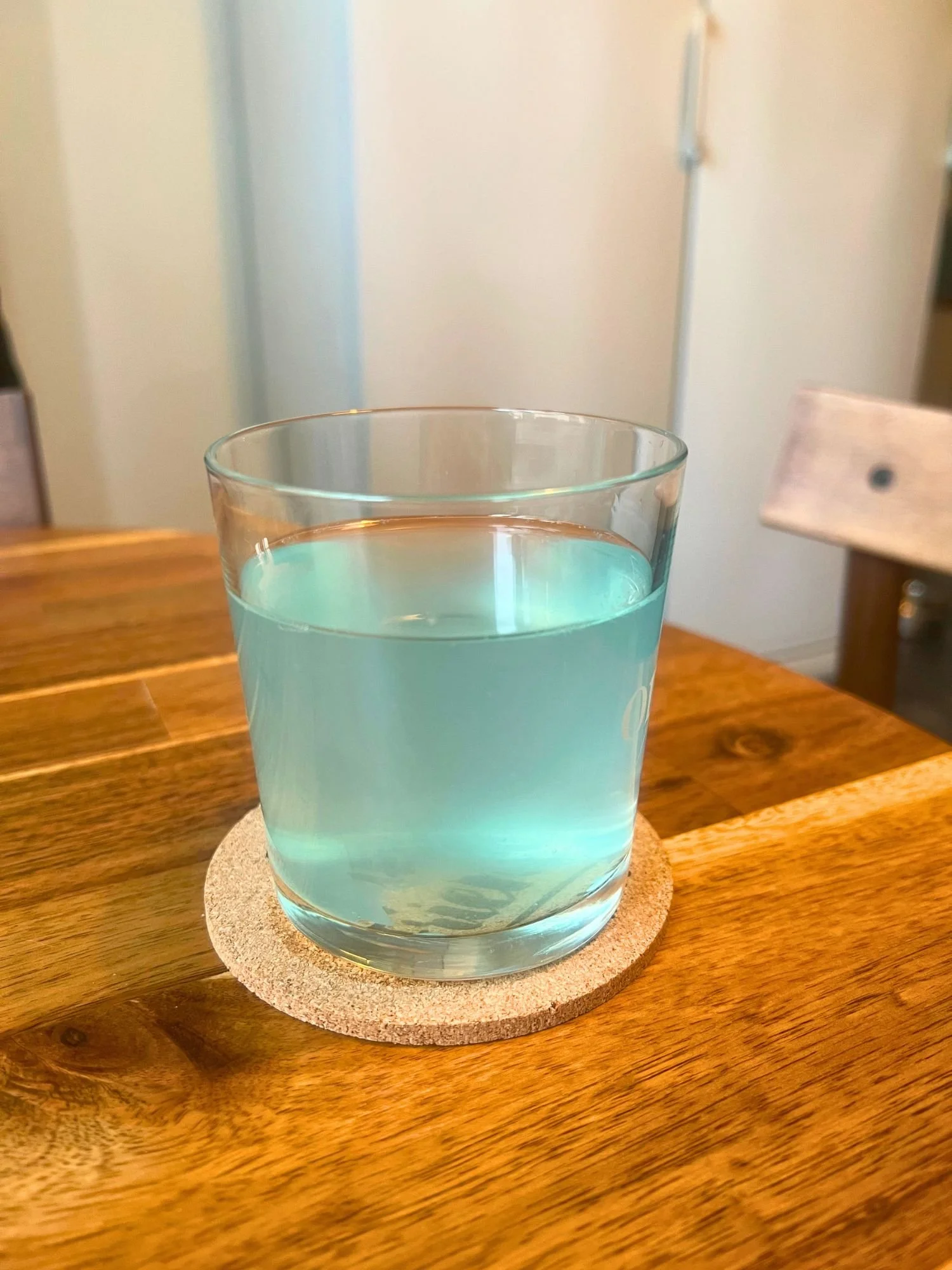 Glass of light blue cocktail on a coaster on a wooden table.
