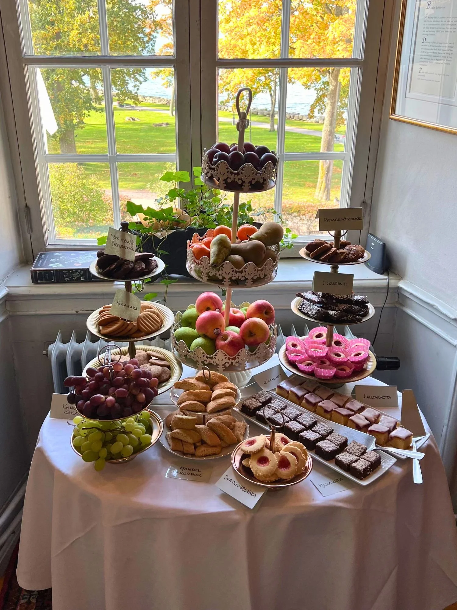 A round table covered in a white tablecloth with an abundant display of fruit and cookies at afternoon tea at Vadstena Klosterhotel.