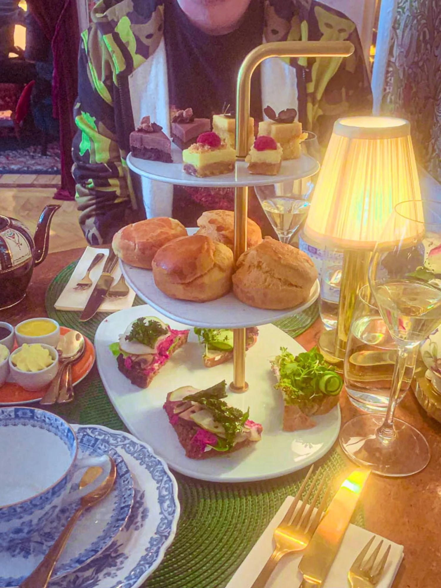 A brightly lit three-tiered afternoon tea service at Alice och Kattens Tesalong in Lund. The top tier has an assortment of miniature sweets, including chocolate cake topped with walnuts and yellow cake garnished with fresh raspberries.