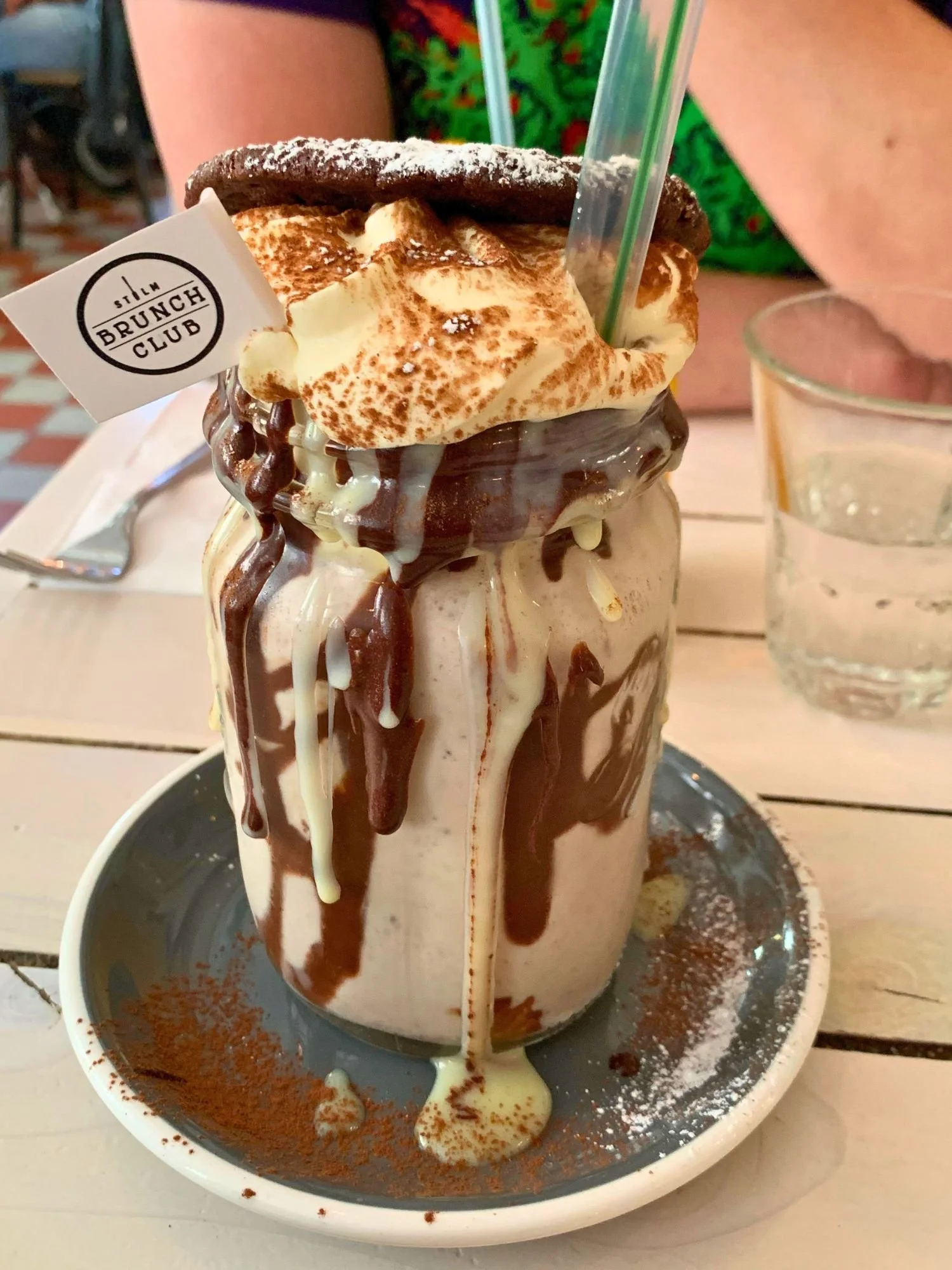 An overflowing chocolate freakshake in a mason jar topped with whipped cream, a chocolate cookie, and a Sthlm Brunch Club flag.
