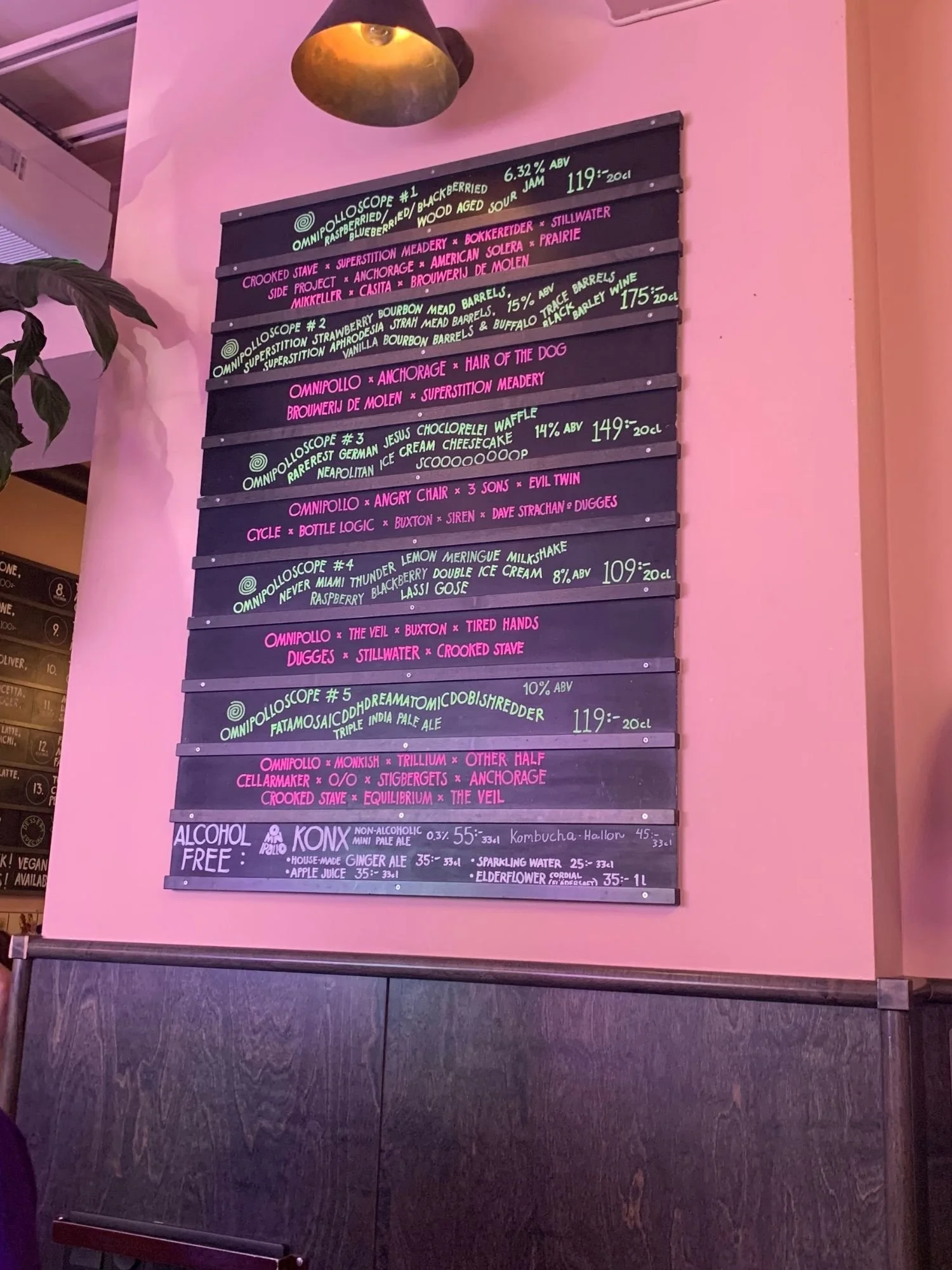 A tall, black menu board mounted on a pink wall displays a list of draft beers labeled Omnipolloscope #1 through #5 with descriptions, collaborator brewery names, ABV percentages, and prices.