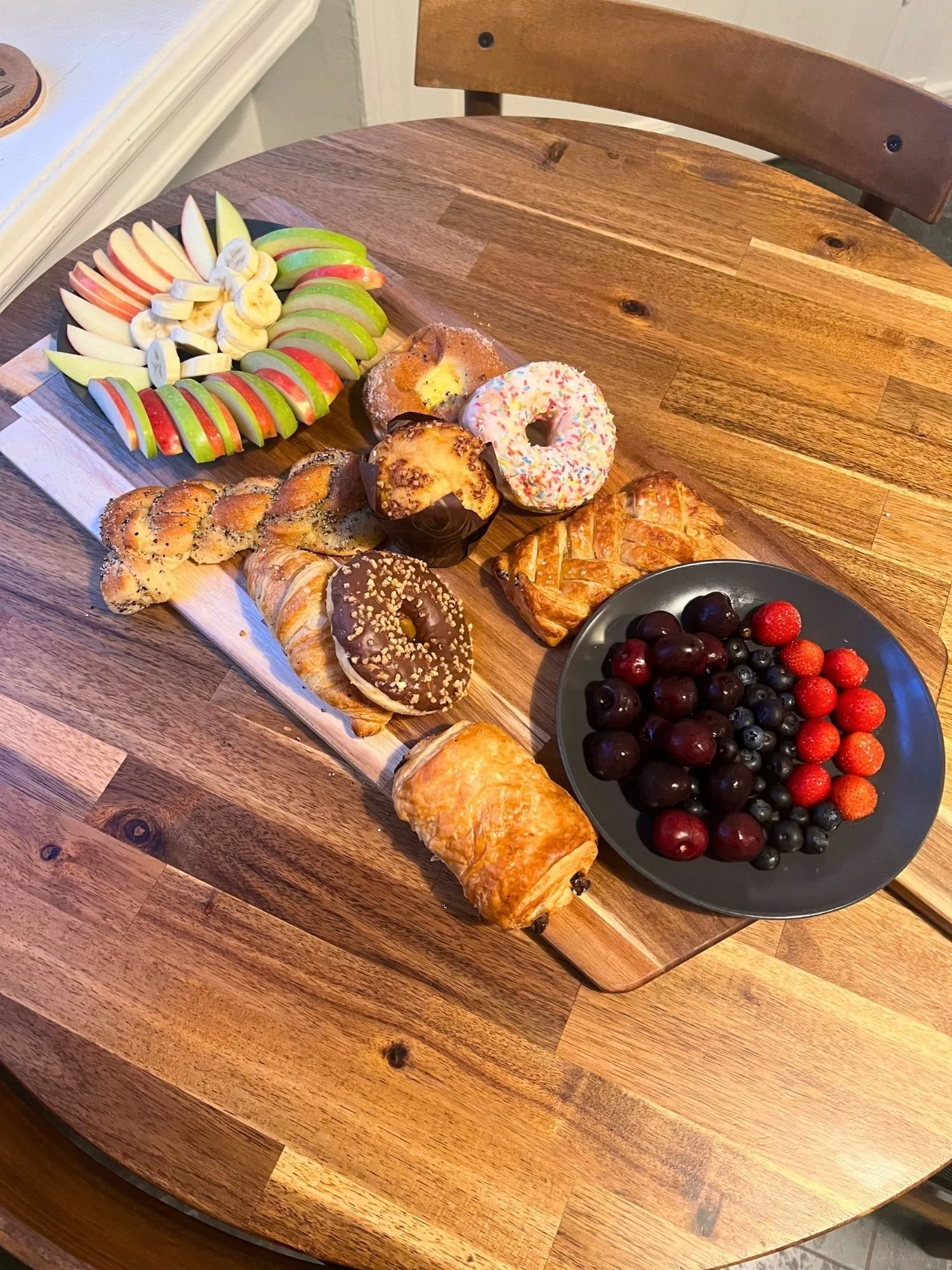 High-angle shot of a long wooden serving board on a round wooden table, featuring an array of pastries.