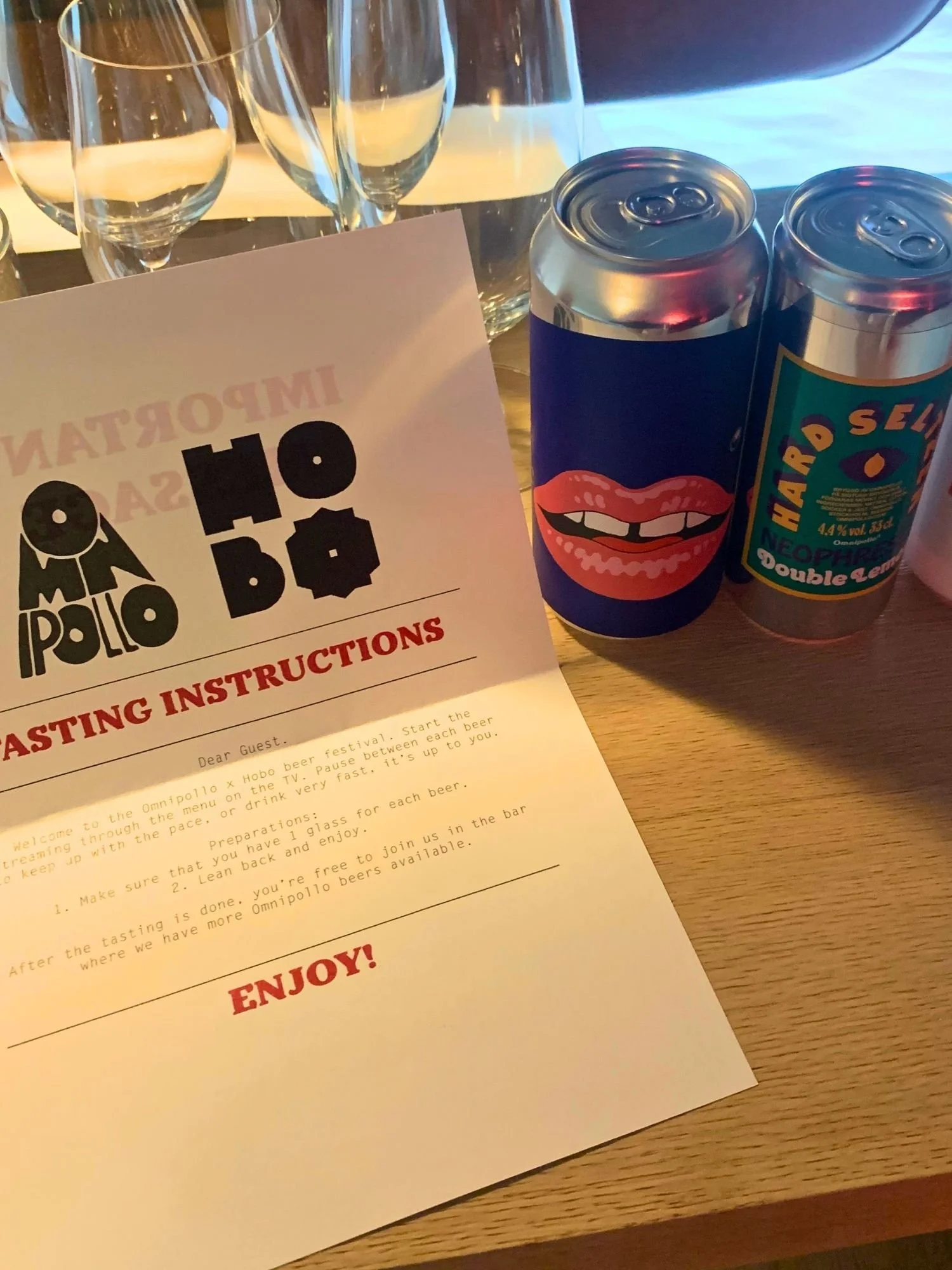 A printed paper sheet titled "TASTING INSTRUCTIONS" with the logos for Omnipollo and Hobo set on a wooden table next to two craft beer cans.