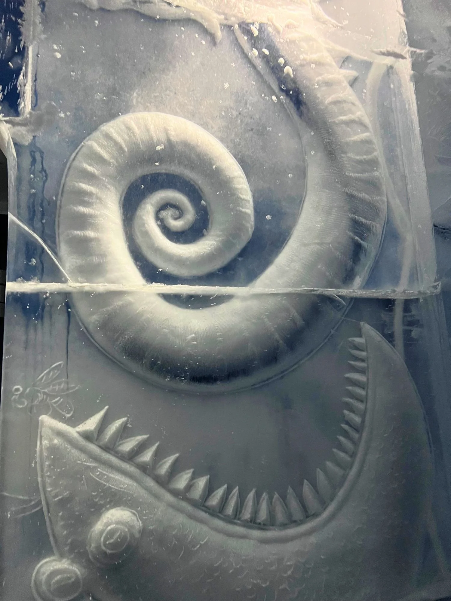 An intricate ice sculpture inside a room at the Icehotel.  The sculpture, carved into a thick slab of translucent, blue-tinted ice, features a whimsical, prehistoric-looking sea creature with a large, gaping mouth full of sharp, triangular teeth.