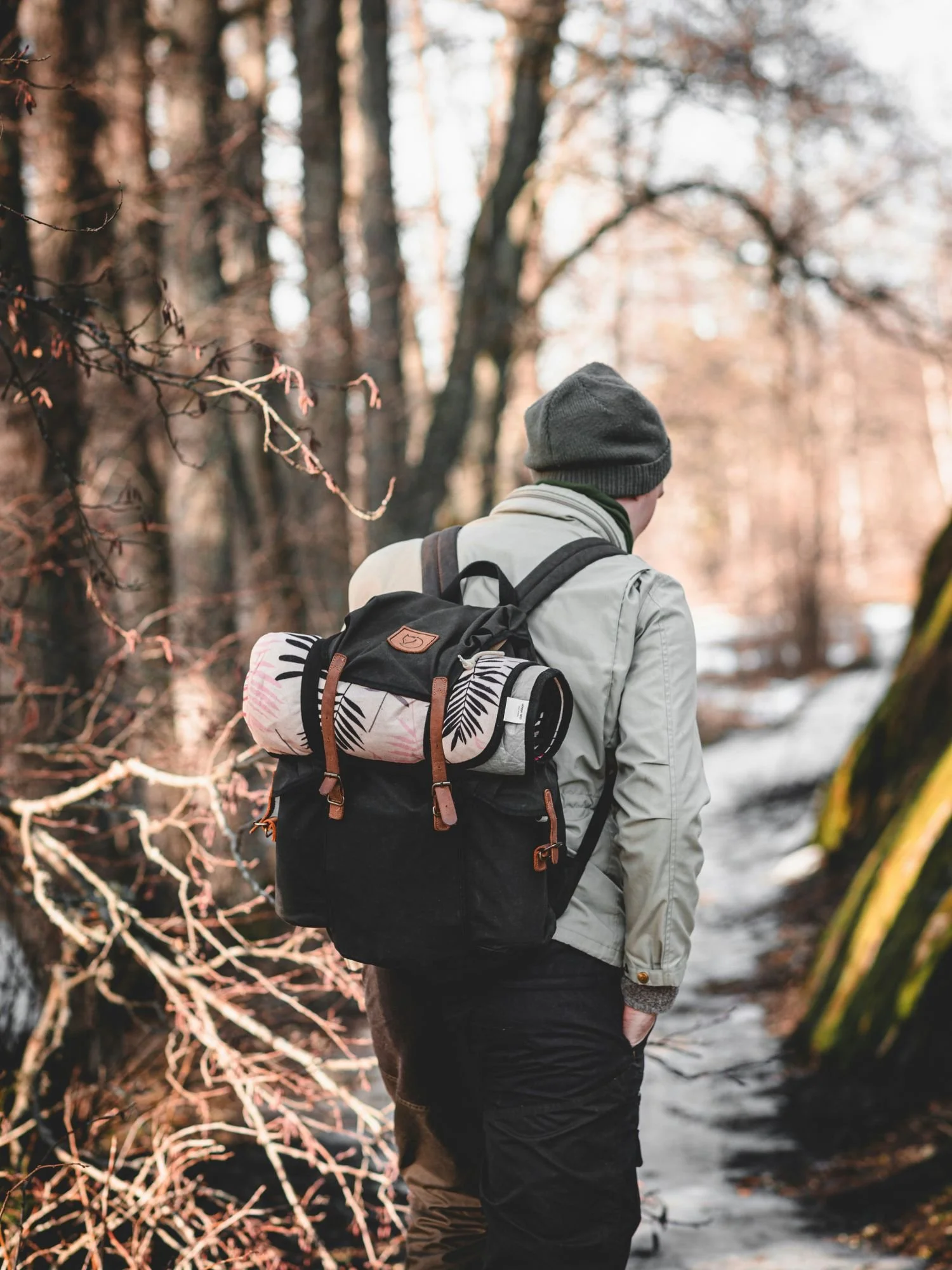 A man viewed from behind hikes along a snow-dusted forest path in Tyresta National Park. He is wearing a grey beanie, a light jacket, and dark trousers.