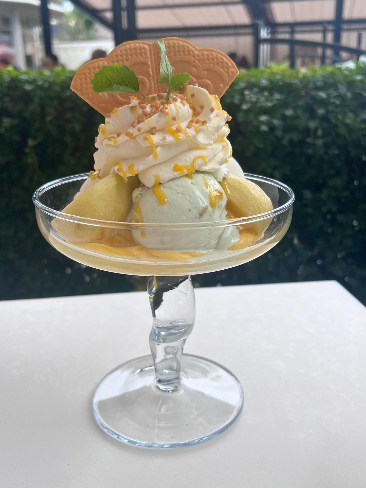 A pear ice cream sundae in a clear stemmed glass topped with sliced fruit, whipped cream, yellow syrup, and a fan wafer cookie.