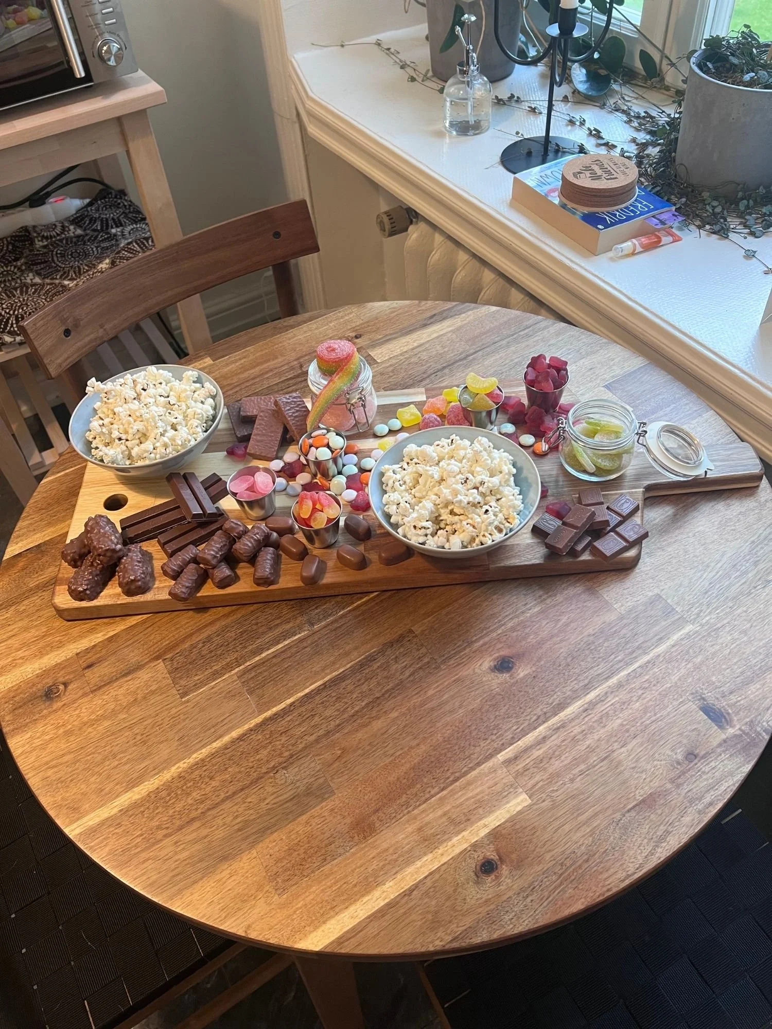 Movie night snack board with popcorn, assorted candy, chocolate bars, and chocolate-covered treats arranged on a wooden serving board.