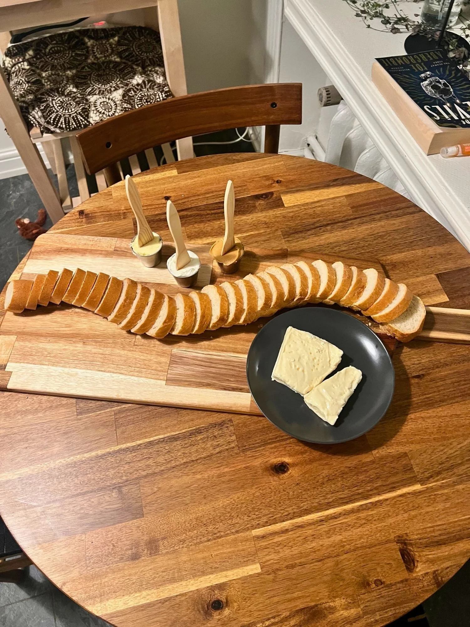 Sliced baguette arranged on a wooden board with three spreads and a plate of soft cheese, ready to serve as a vegetarian charcuterie board.