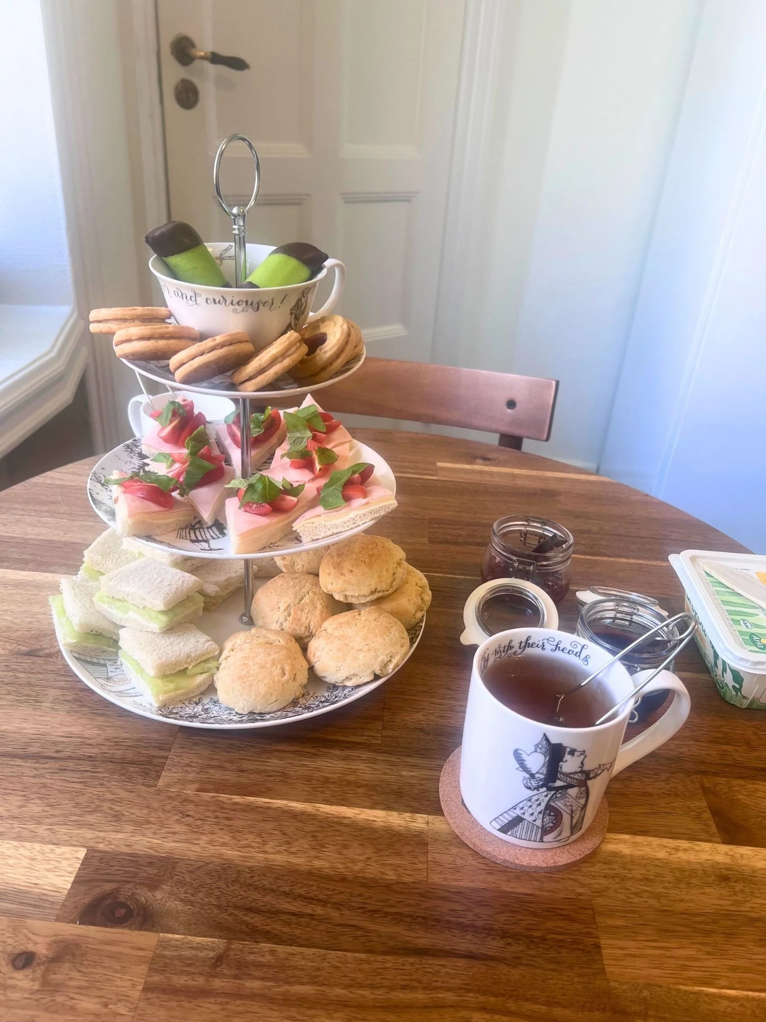 A three-tiered tea stand filled with treats and sandwiches on a wooden table.