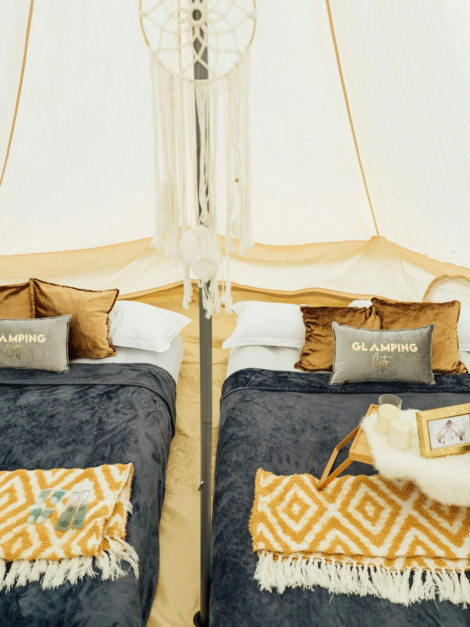 The symmetrical interior of a white canvas glamping bell tent featuring two single beds arranged side-by-side, separated by a central metal tent pole.
