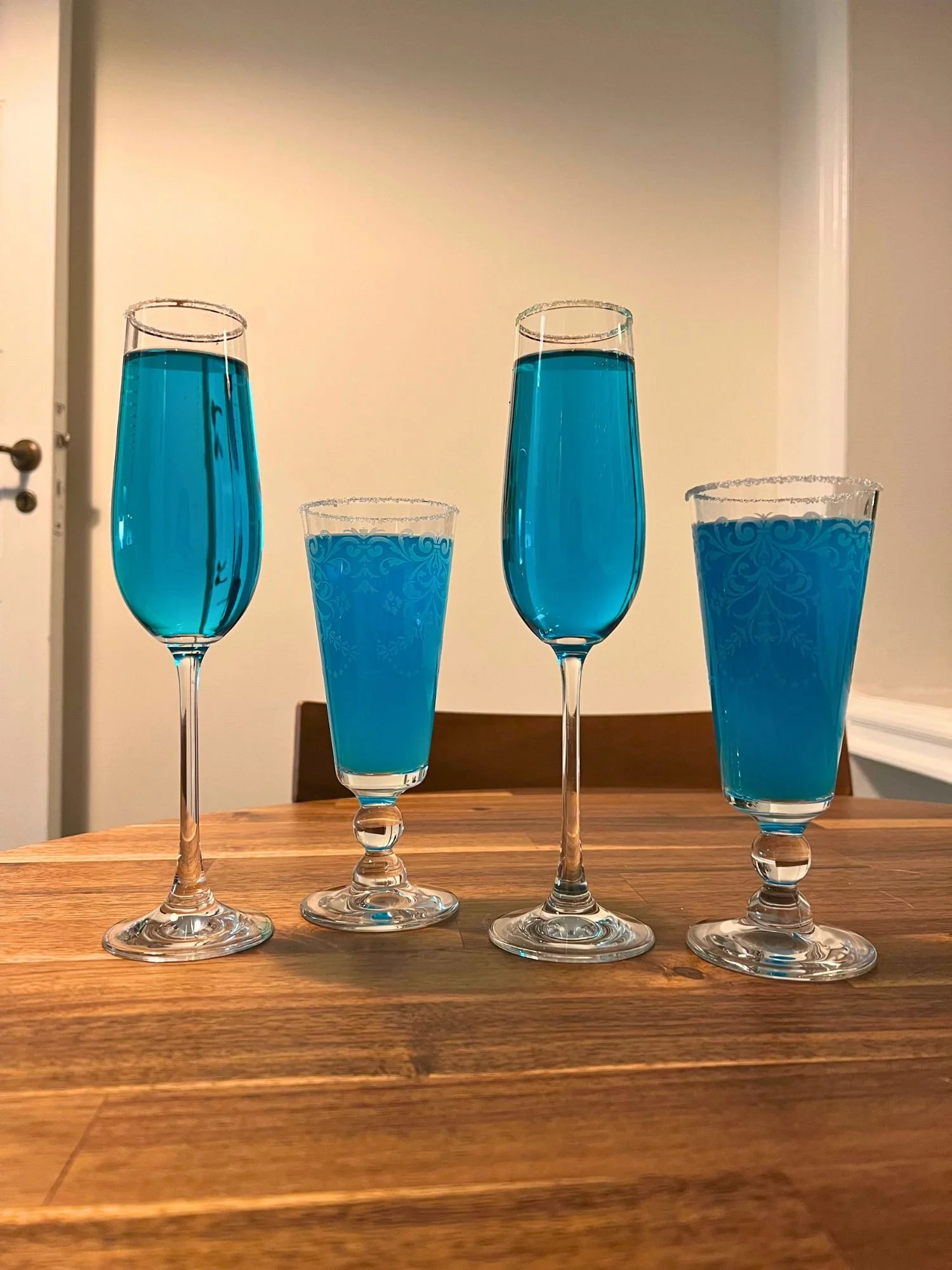 Four sugar-rimmed champagne glasses filled with bright blue cocktails arranged on a wooden table.