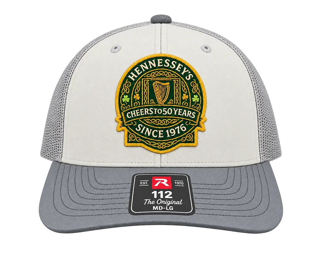 White and gray trucker hat with a green and gold embroidered Hennessey’s patch reading “Cheers to 50 Years” and “Since 1976.”