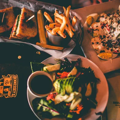 Top view of a salad on a white plate, sandwich cut in half with french fries in a basket with parchment paper, and white plate with sliced eggs.