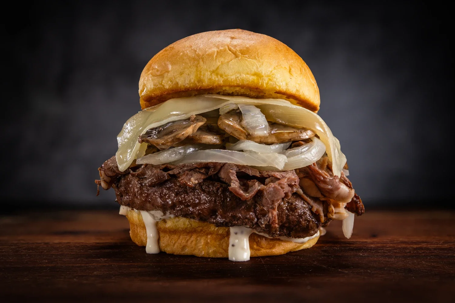 Close-up of a French Dip Burger with prime rib, Swiss cheese, grilled onions, sautéed mushrooms, and horseradish crème on a toasted bun.