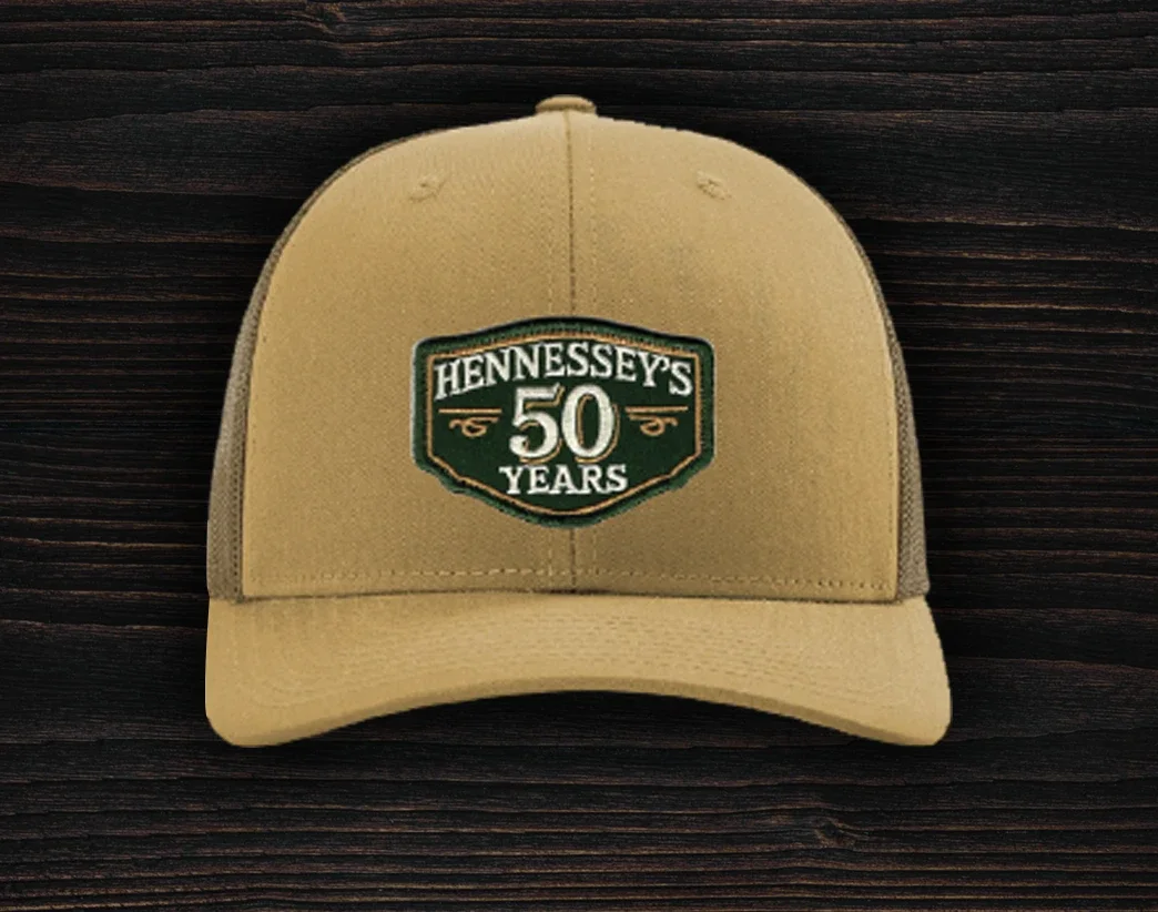 Camel trucker hat featuring an embroidered Hennessey’s Tavern 50 Years anniversary logo patch on the front panel.