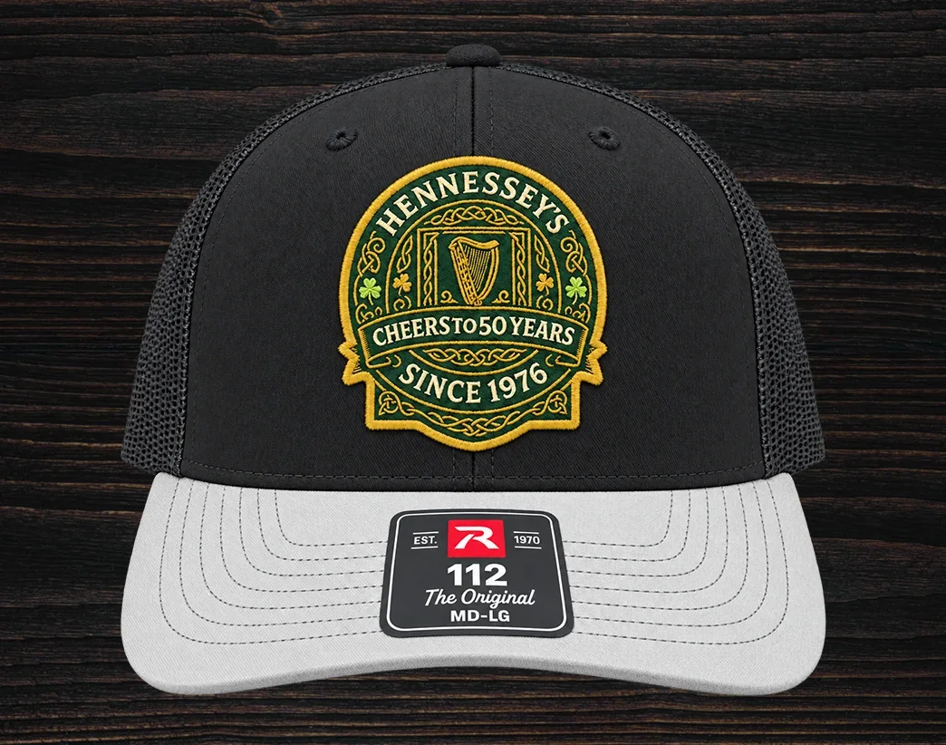Black and white trucker hat featuring an embroidered Hennessey’s Tavern Cheers to 50 Years anniversary logo patch on the front panel