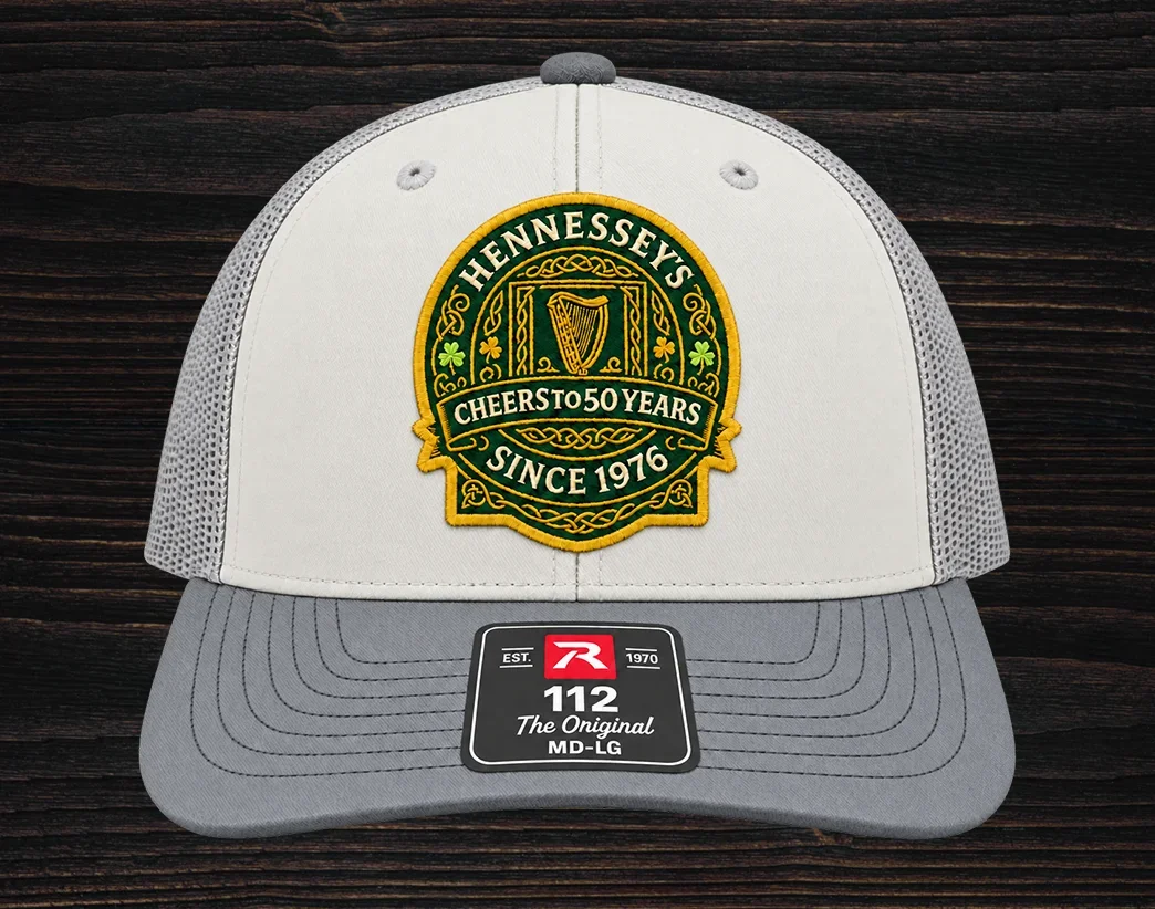 White and gray trucker hat featuring an embroidered Hennessey’s Tavern Cheers to 50 Years anniversary logo patch on the front panel