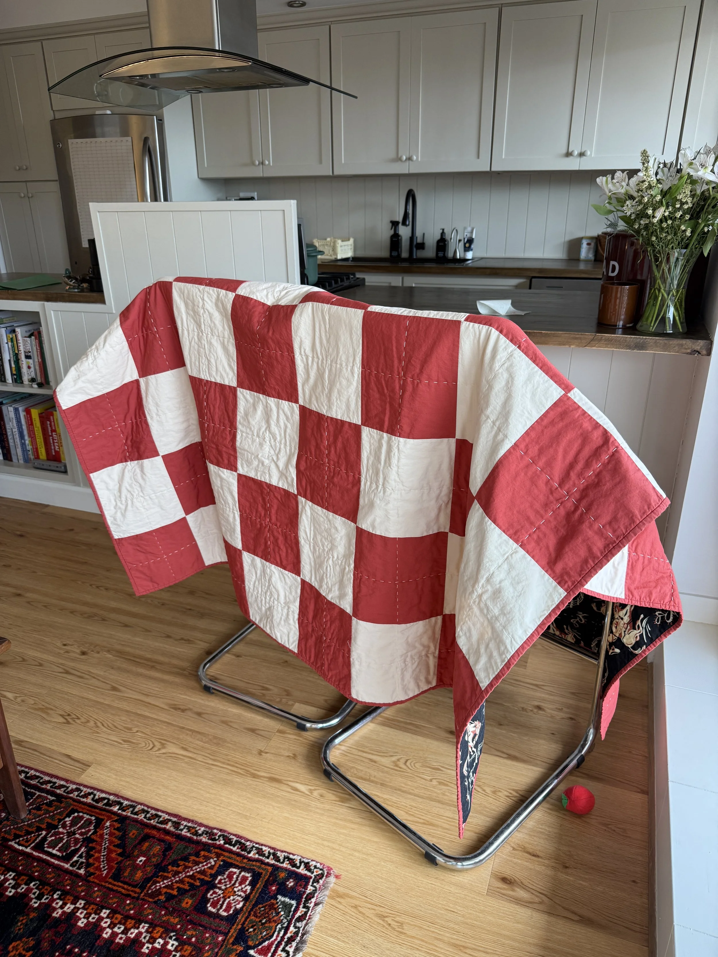 a patchwork quilt in cream and a burnt sienna color draped over two stools in a New York City apartment kitchen counter