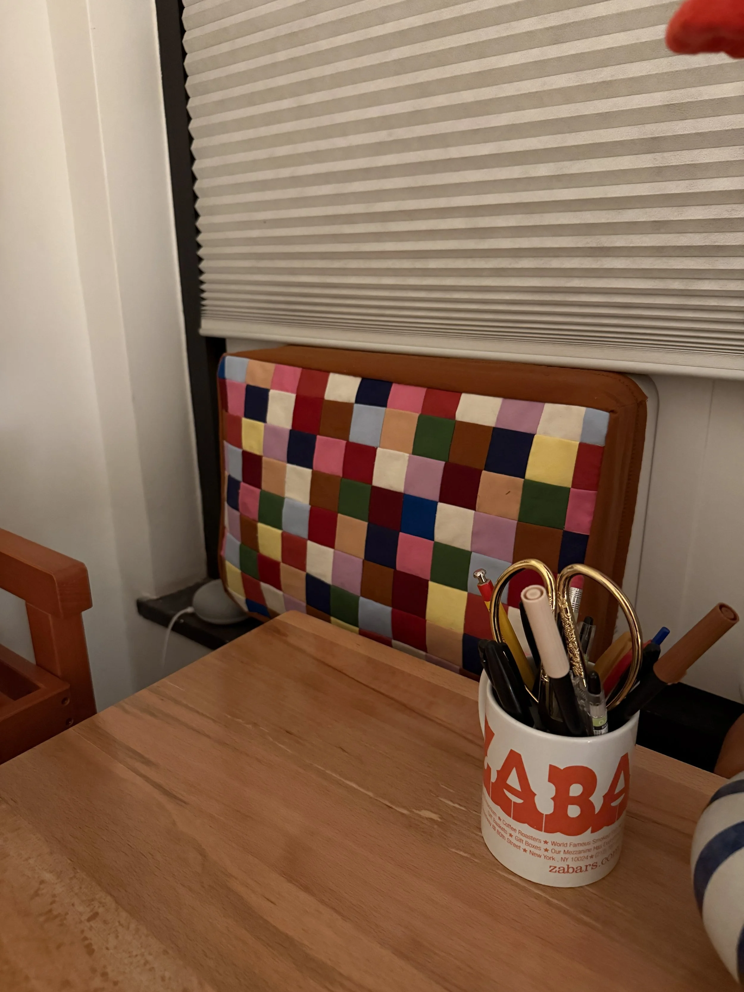 A New York City apartment window with a window air conditioner. The a/c is covered in a DIY patchwork quilt style cover to keep air from coming in