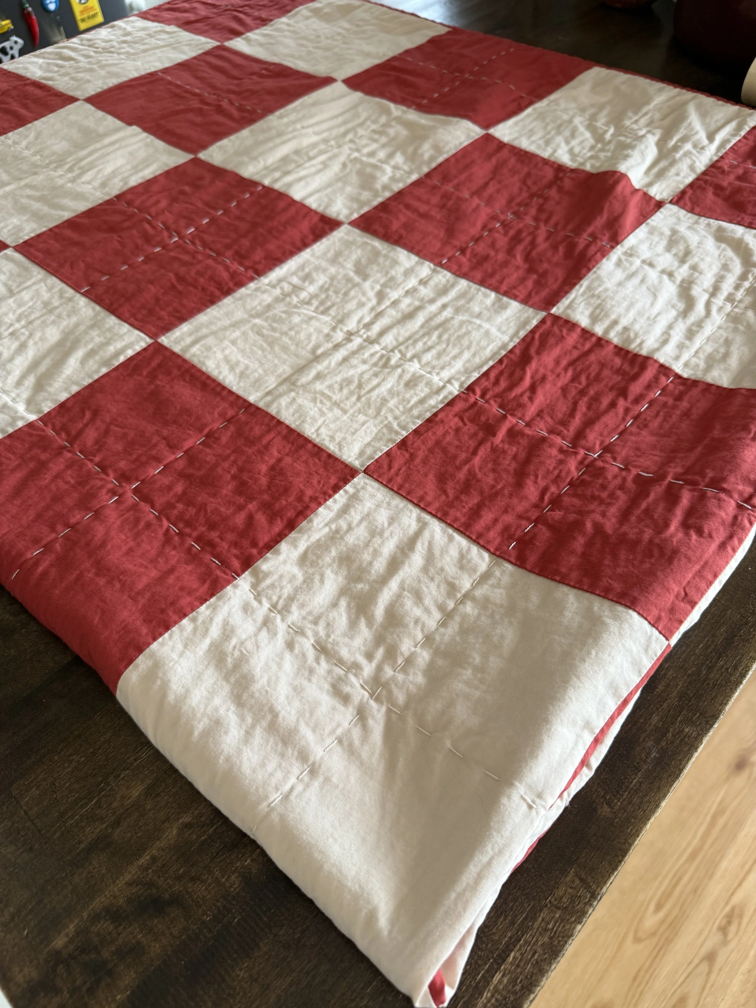 a patchwork quilt in cream and a burnt sienna color folded on a butcher block countertop