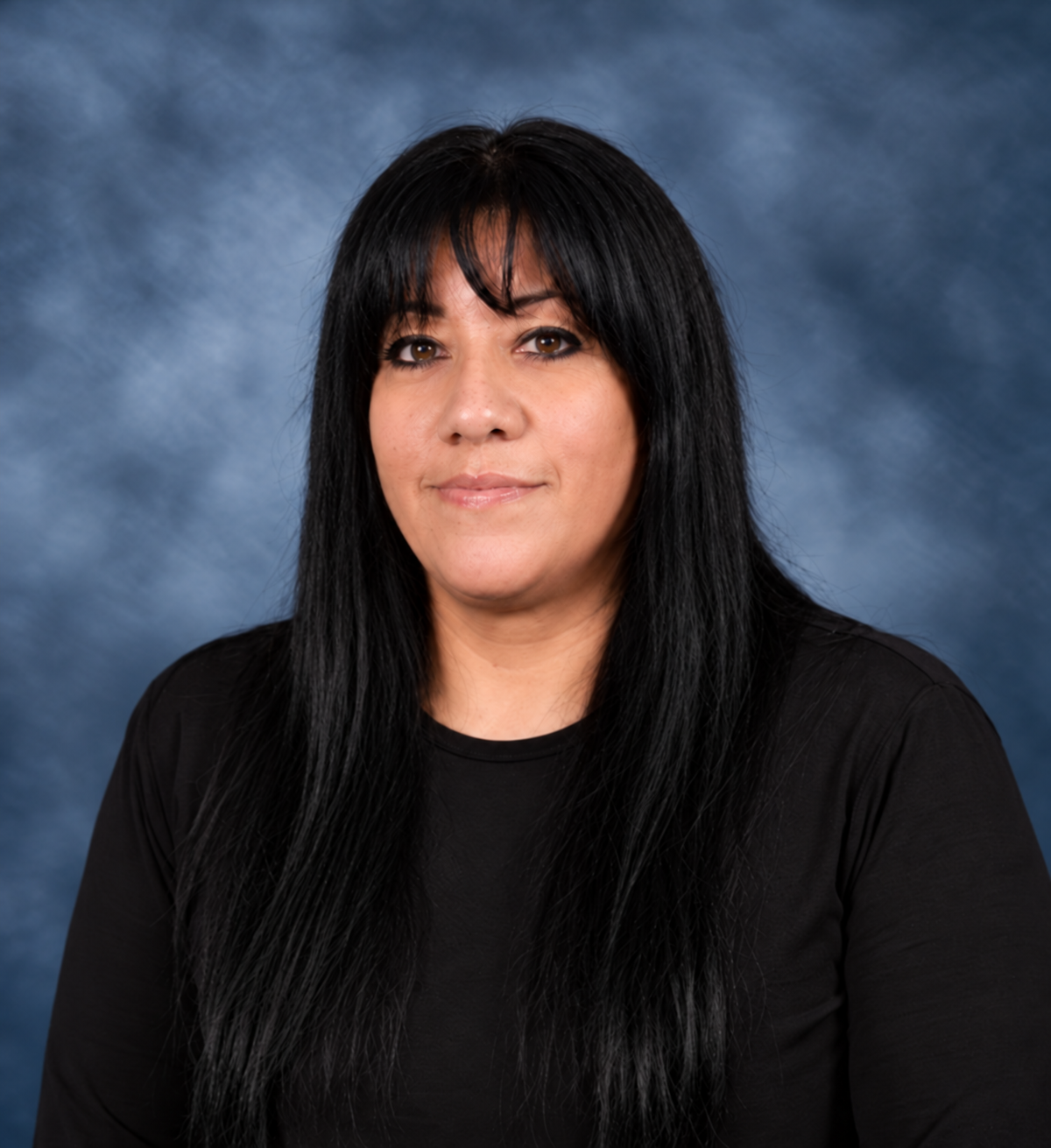 Portrait of a woman with long black hair and bangs, wearing a black top, against a blue-gray background.