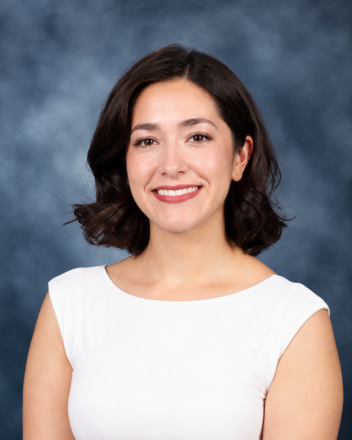 Portrait of a smiling woman with shoulder-length dark hair, wearing a sleeveless white top, against a dark blue and gray background.