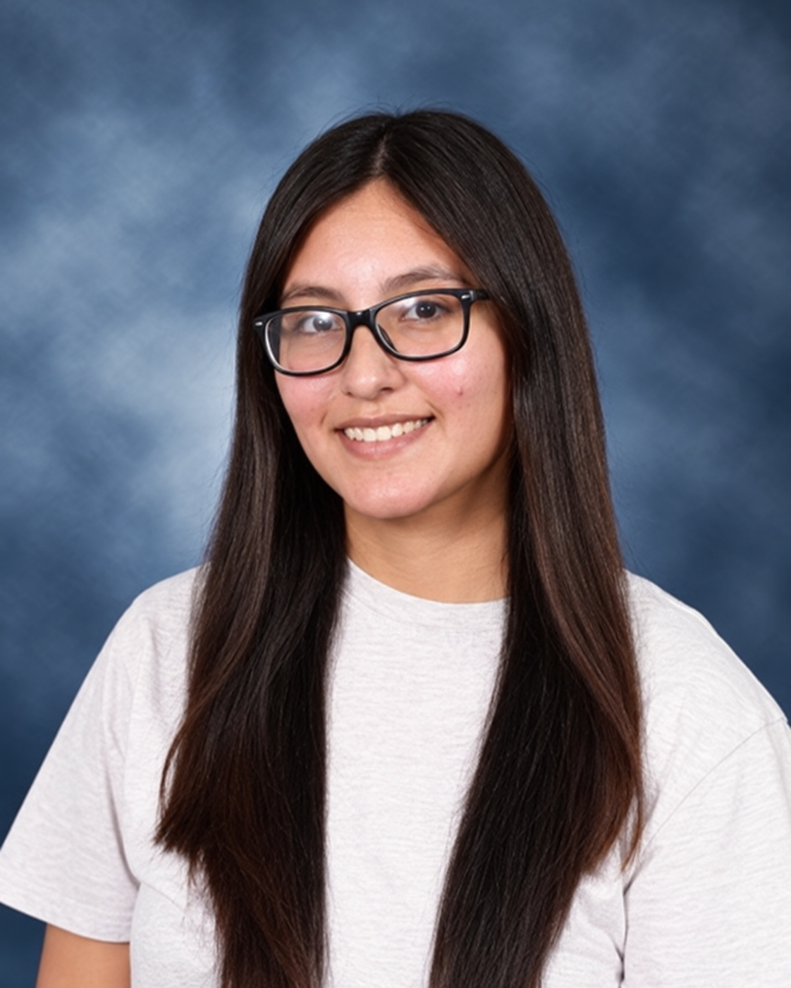 A young woman with long dark hair, wearing glasses and a white t-shirt, smiling against a blue cloudy background.