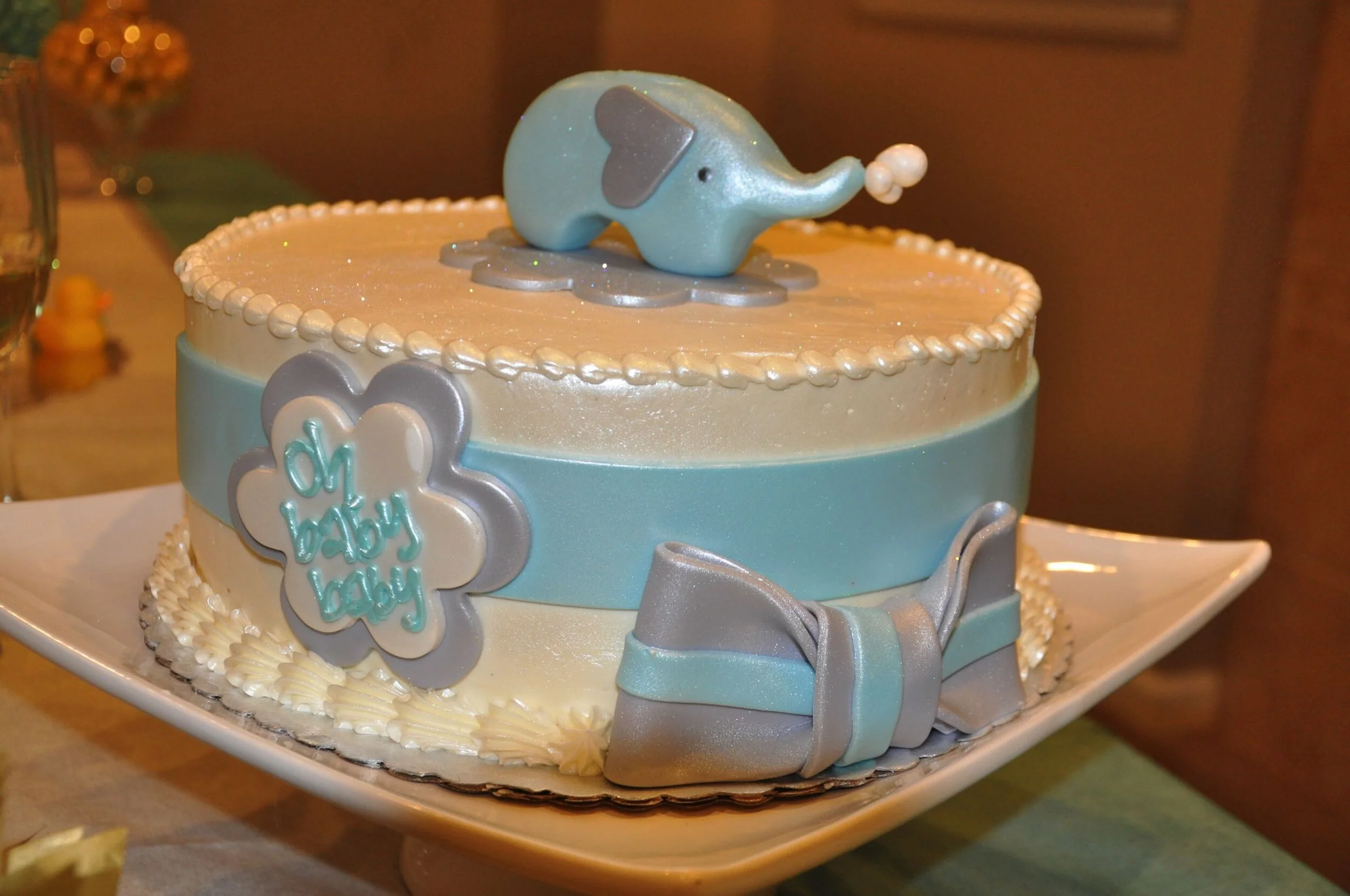 Baby shower cake decorated with an elephant topper and "Oh baby baby" inscription, featuring blue and silver accents.