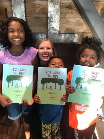 Four children holding books and smiling in front of a wooden wall.