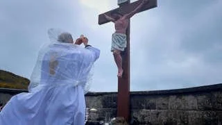 Fr Gerry McCloskey raises the host before a coastal crucifix