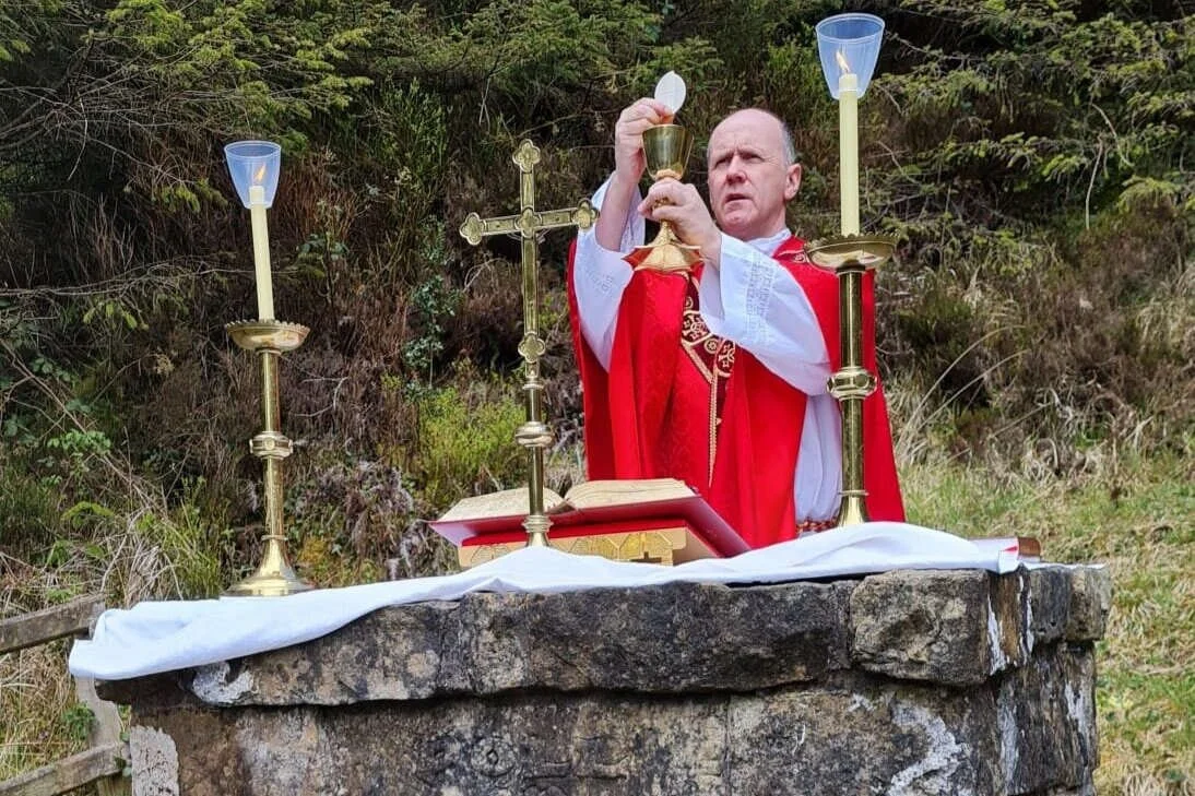 Fr Sean Mulligan raises the host at a woodland Mass Rock