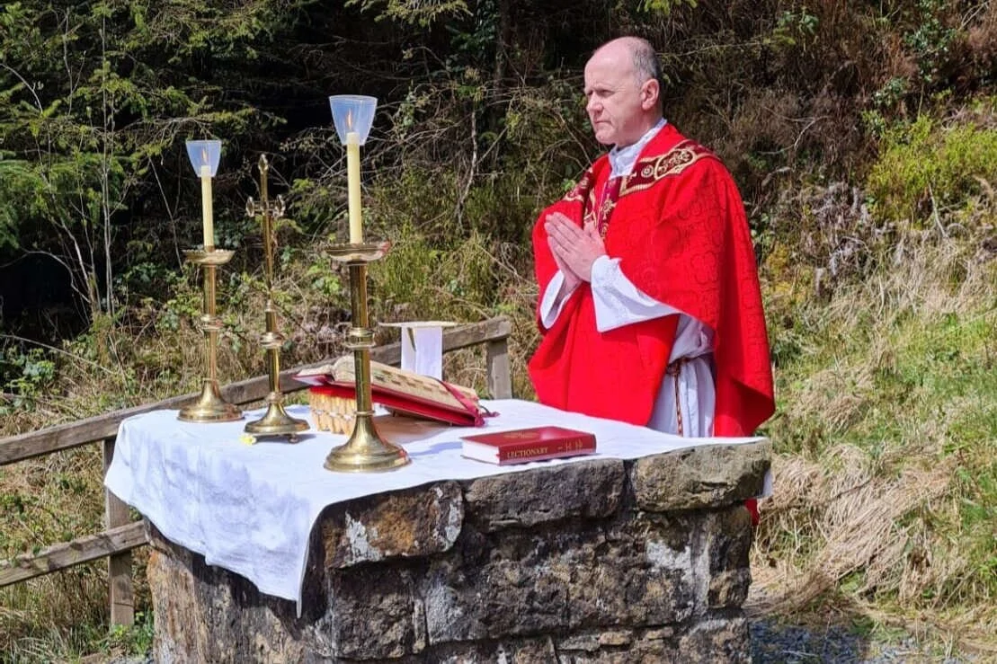Fr Sean Mulligan prays beside a stone altar in woodland