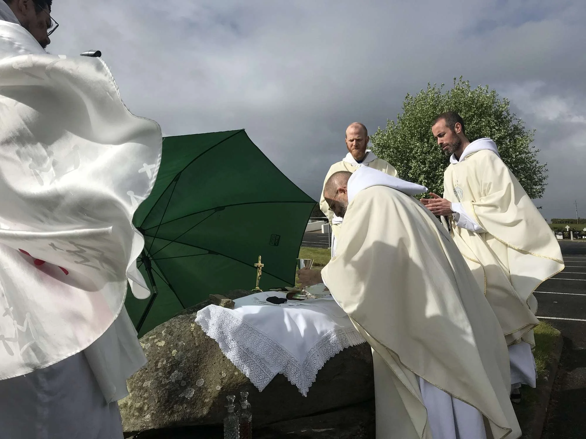 Franciscan friars pray beside a stone altar under an umbrella